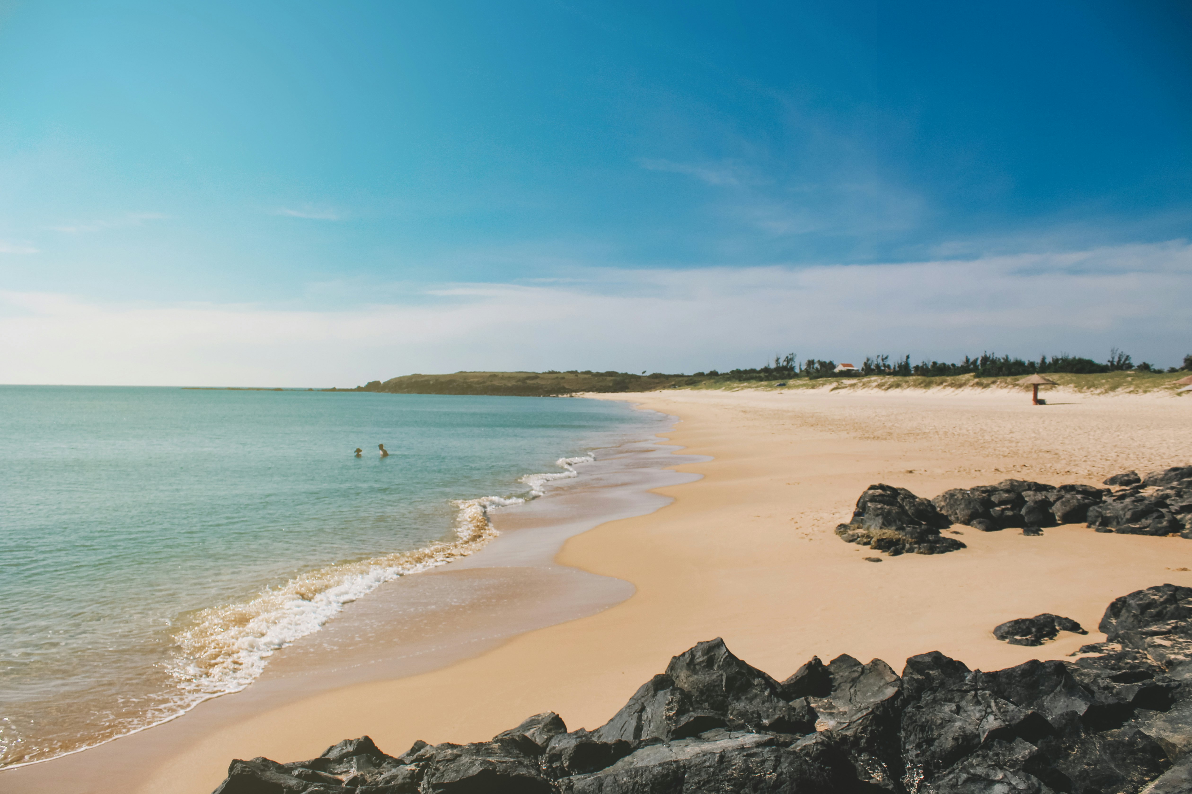 Two people relax in the ocean shallows on a gorgeous golden stretch of sand that is otherwise deserted.