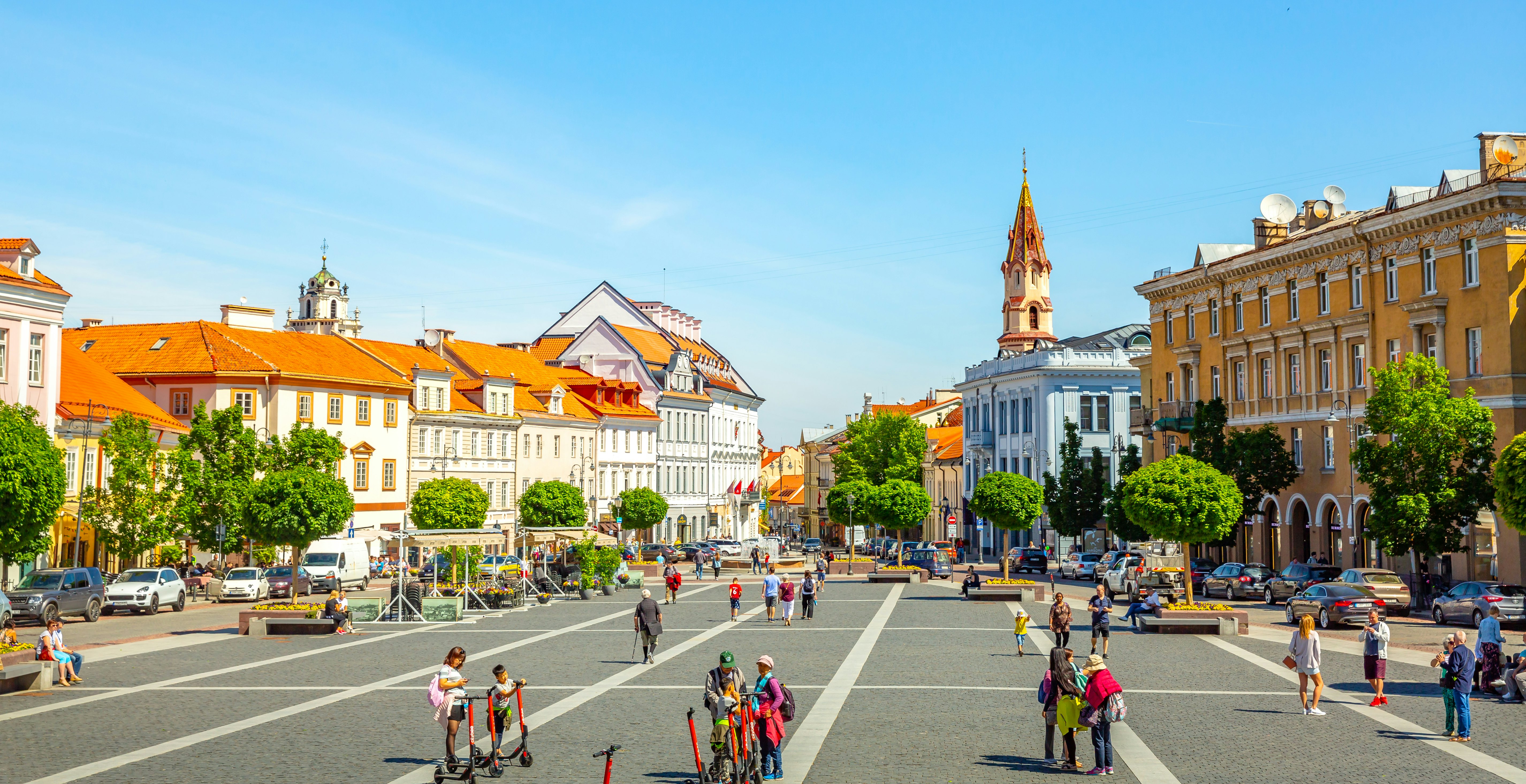 Tourists in a city square lined with medieval buildings and a tall church spire.