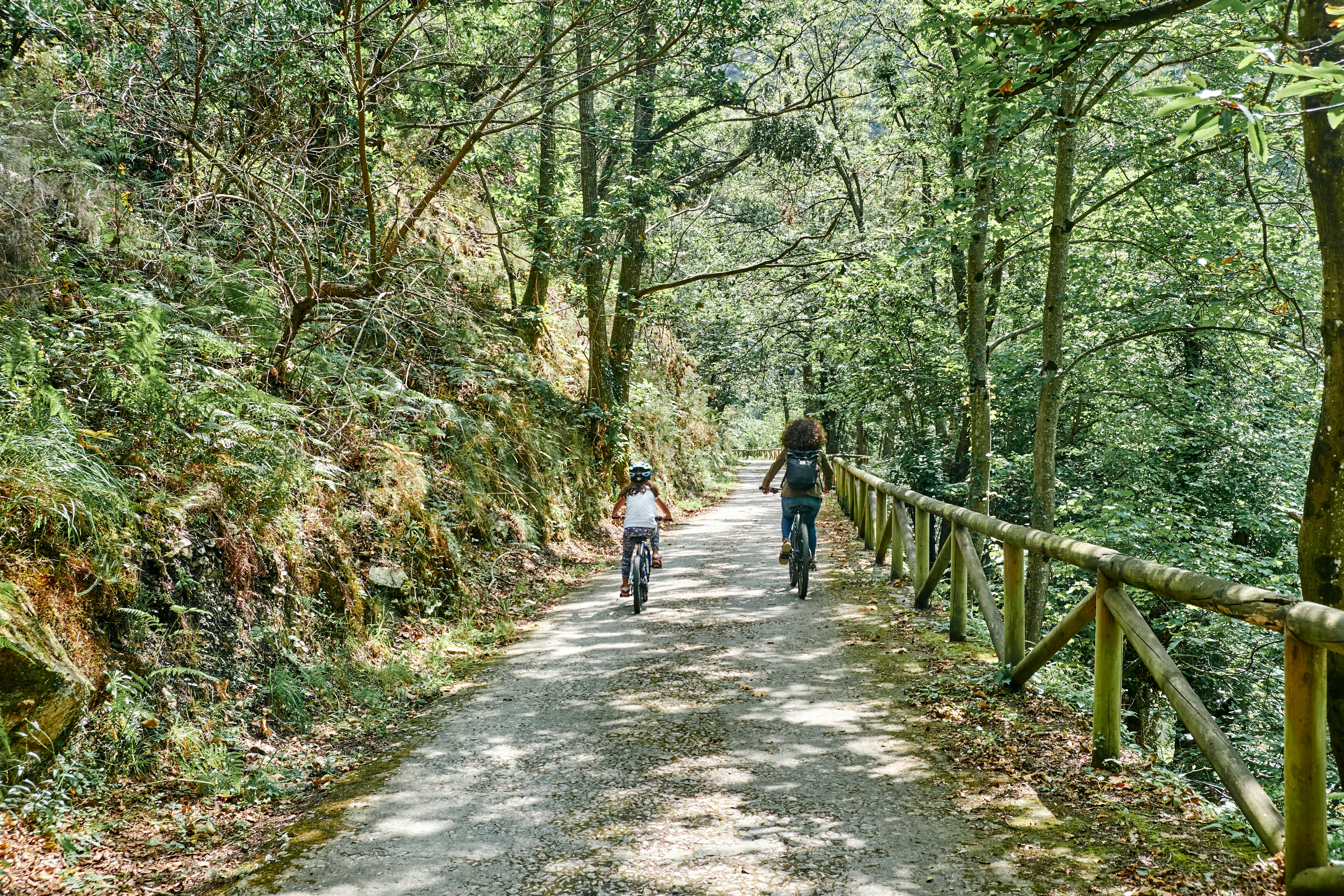 A woman and child cycle in the dappled light on the Bear Path (Senda del Oso) in Asturias, Spain