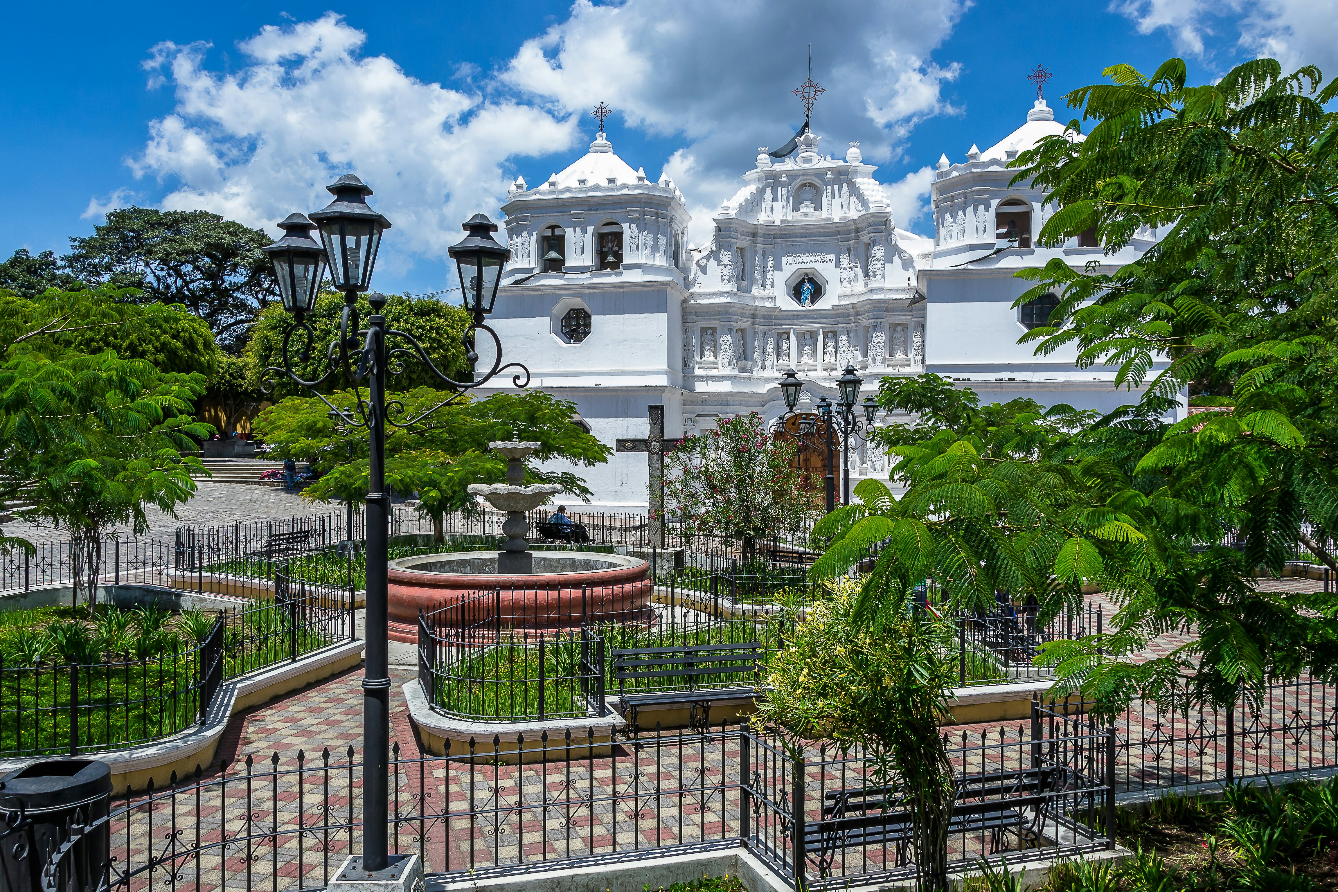 An ornate white church with a iron-fenced brick courtyard in front on a bright, sunny day.