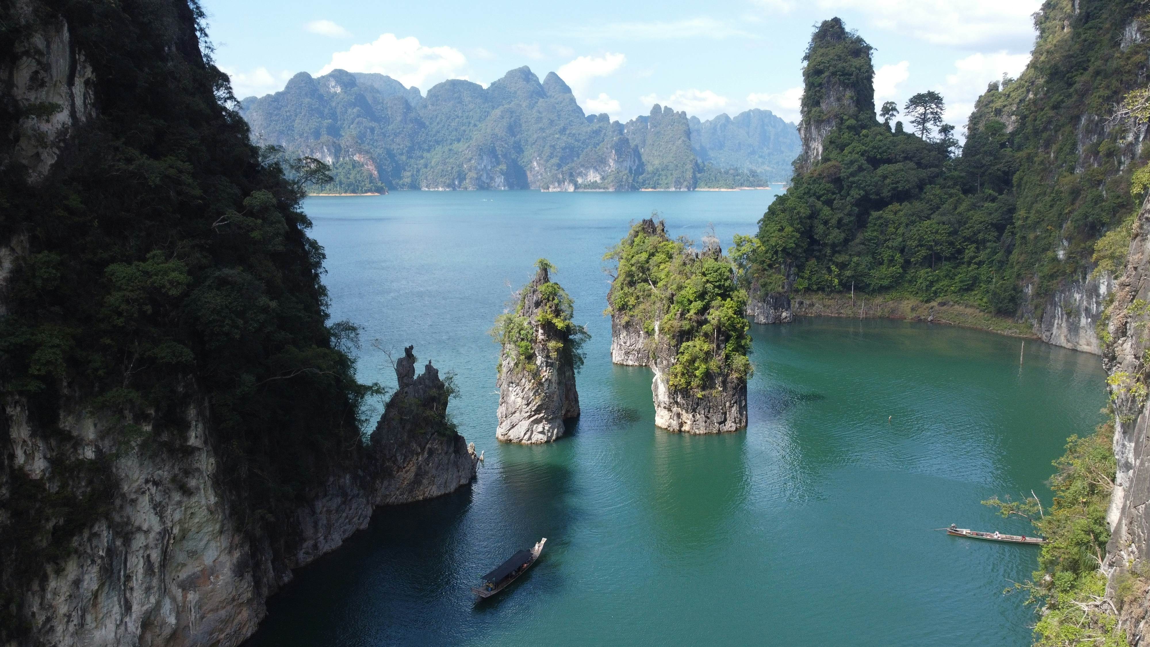Stunning view of Khao Sok National Park in Thailand. Emerald waters of Cheow Larn Lake surrounded by lush rainforest and limestone cliffs. Dramatic landscape showcases Thailand's natural beauty.  License Type: media  Download Time: 2024-04-01T03:04:15.000Z  User: gwencotter  Is Editorial: No  purchase_order: