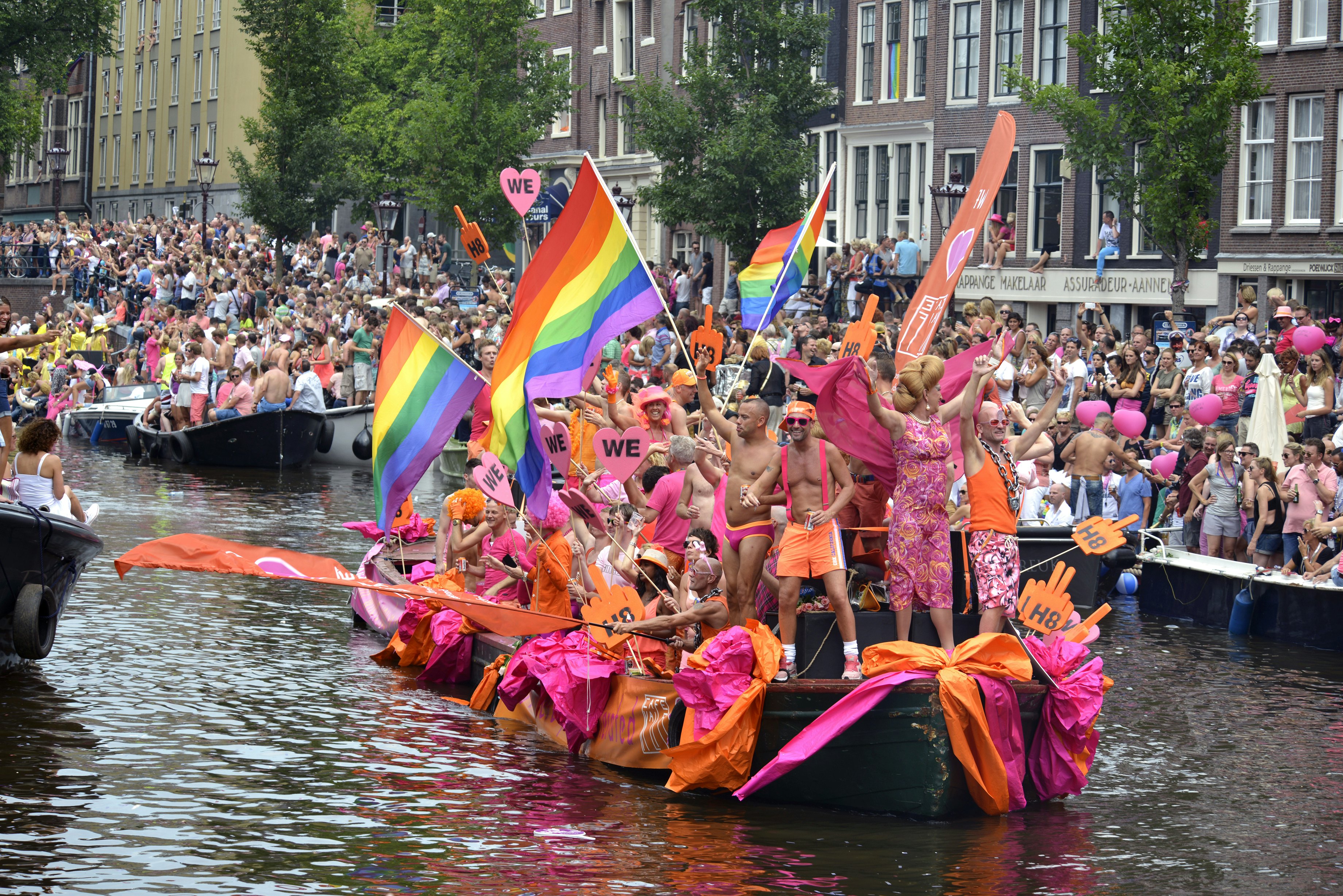 A group of people in pink carrying rainbow flags on the river in Amsterdam.