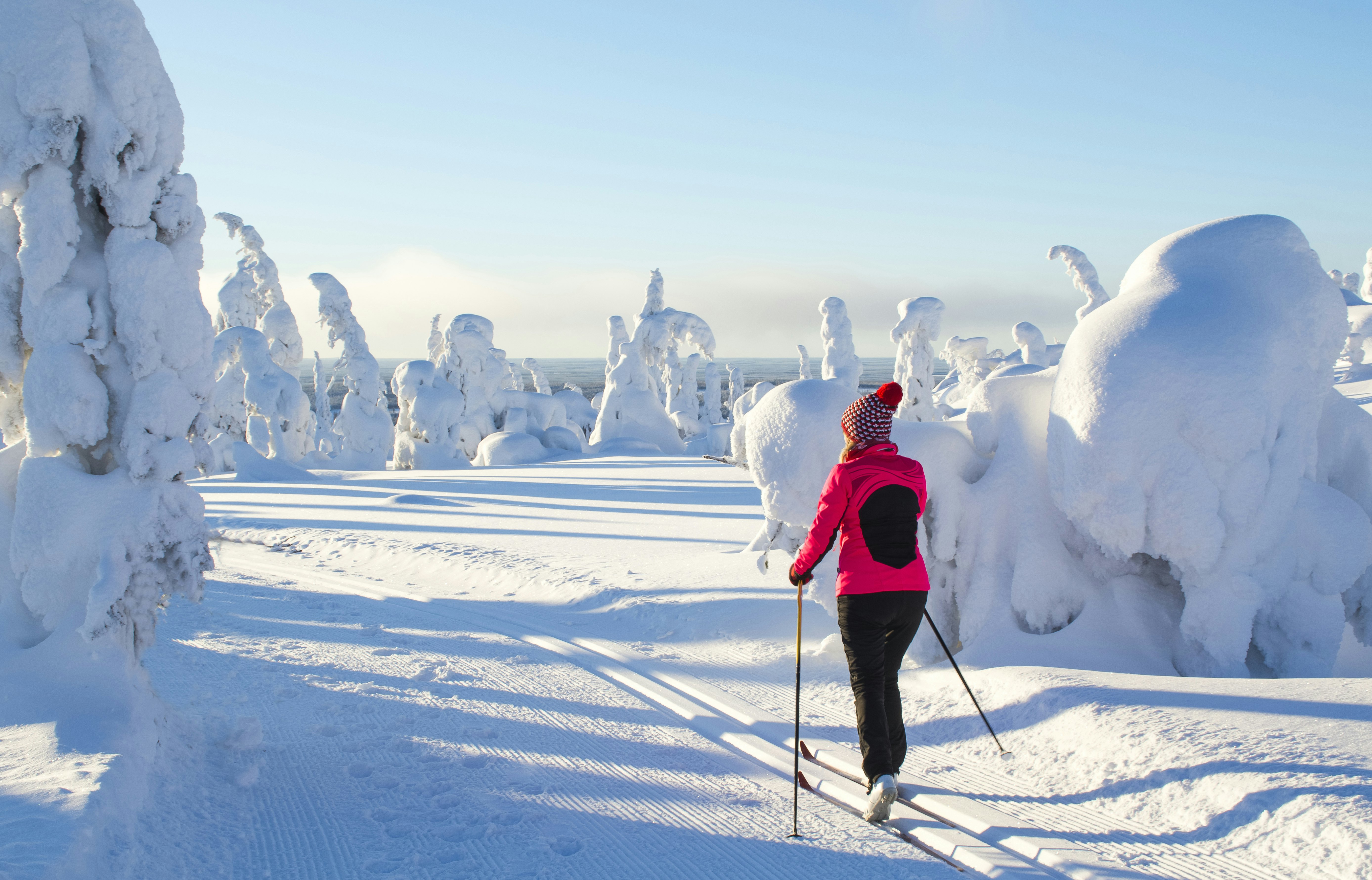 A skier in a pink jacket and black pants in a snow-covered landscape in Finland.