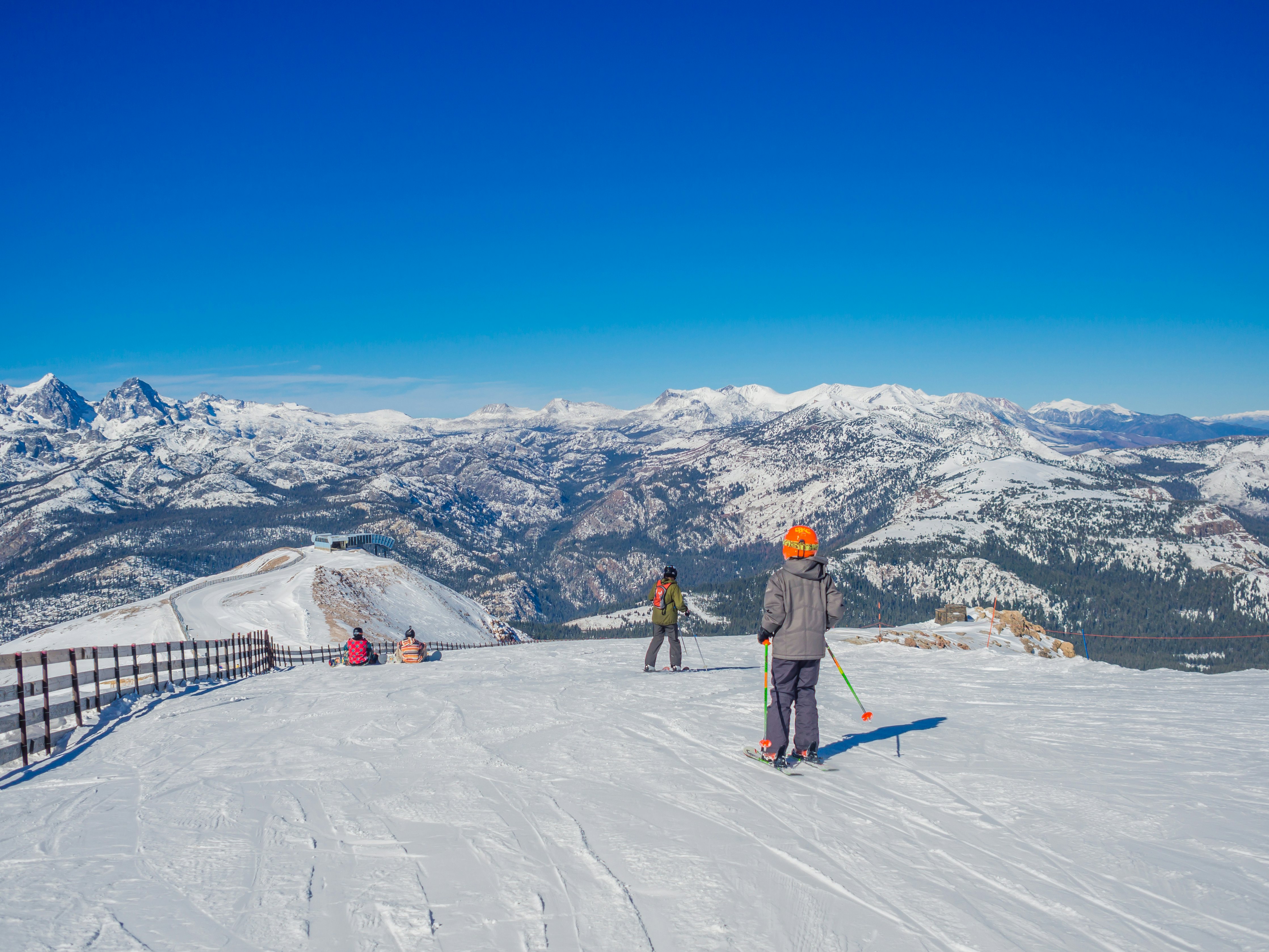 A boy with ski poles looks at the view of the snowy mountain range ahead of him.