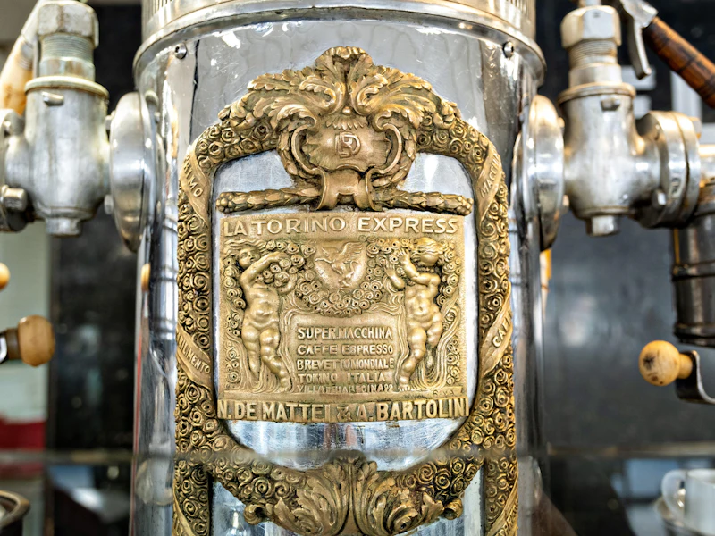 Close-up of old-style espresso machines with a bronze-colored plaque on the front of one reading "La Torino Express."