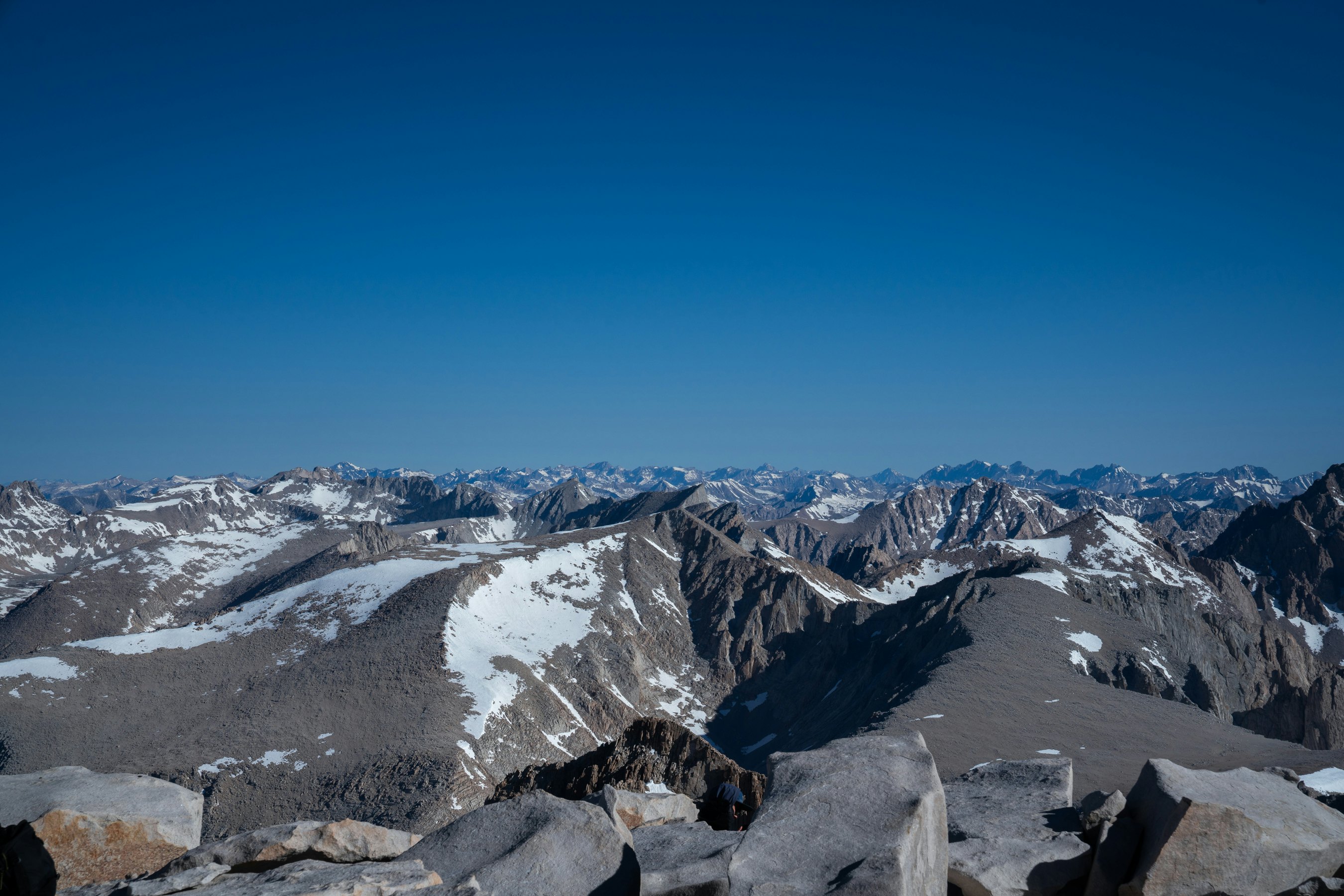 A mountain range stretches into the distance, with snow over escarpments and a blue sky above.