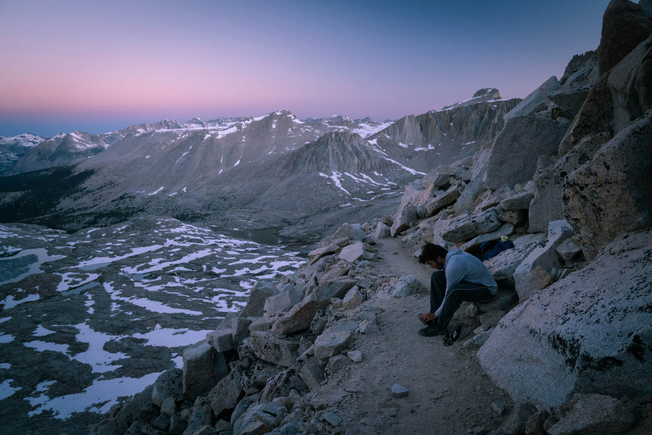 A hiker pauses on the final stretch of a trail to adjust his footwear.