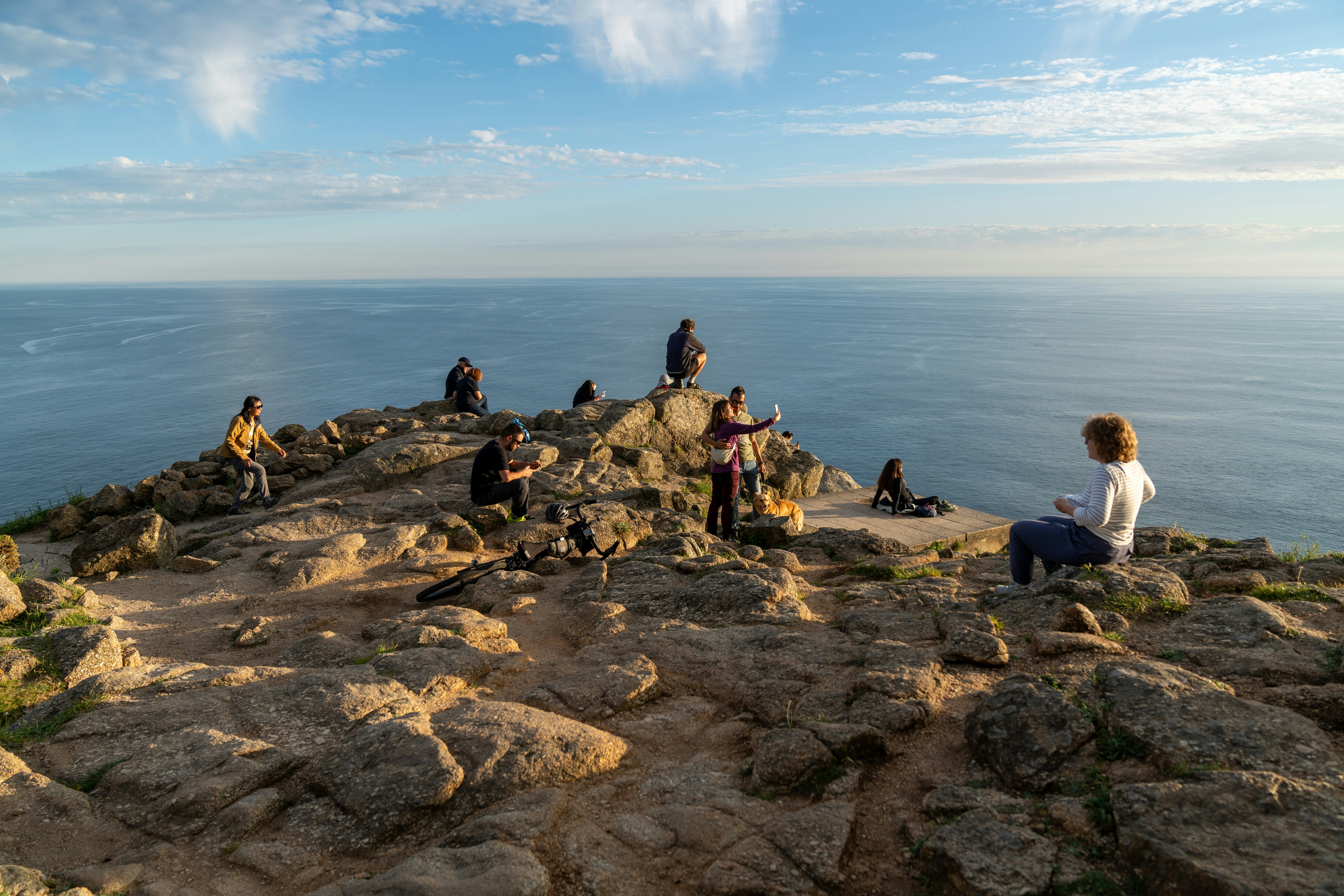 People relaxing and taking photos at Finisterre near the water.