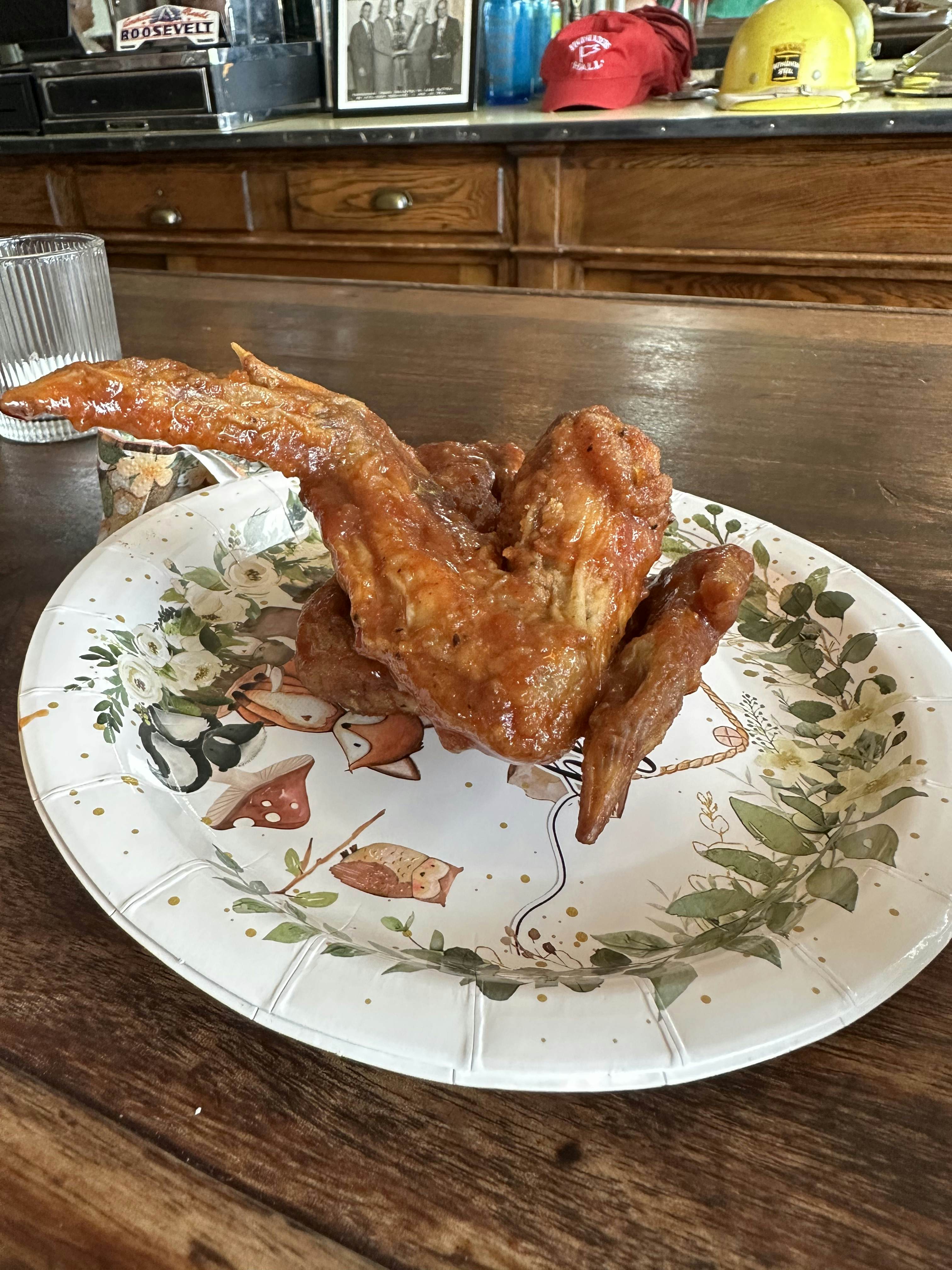 Full sauced buffalo wing on a white with green leaf paper plate. 