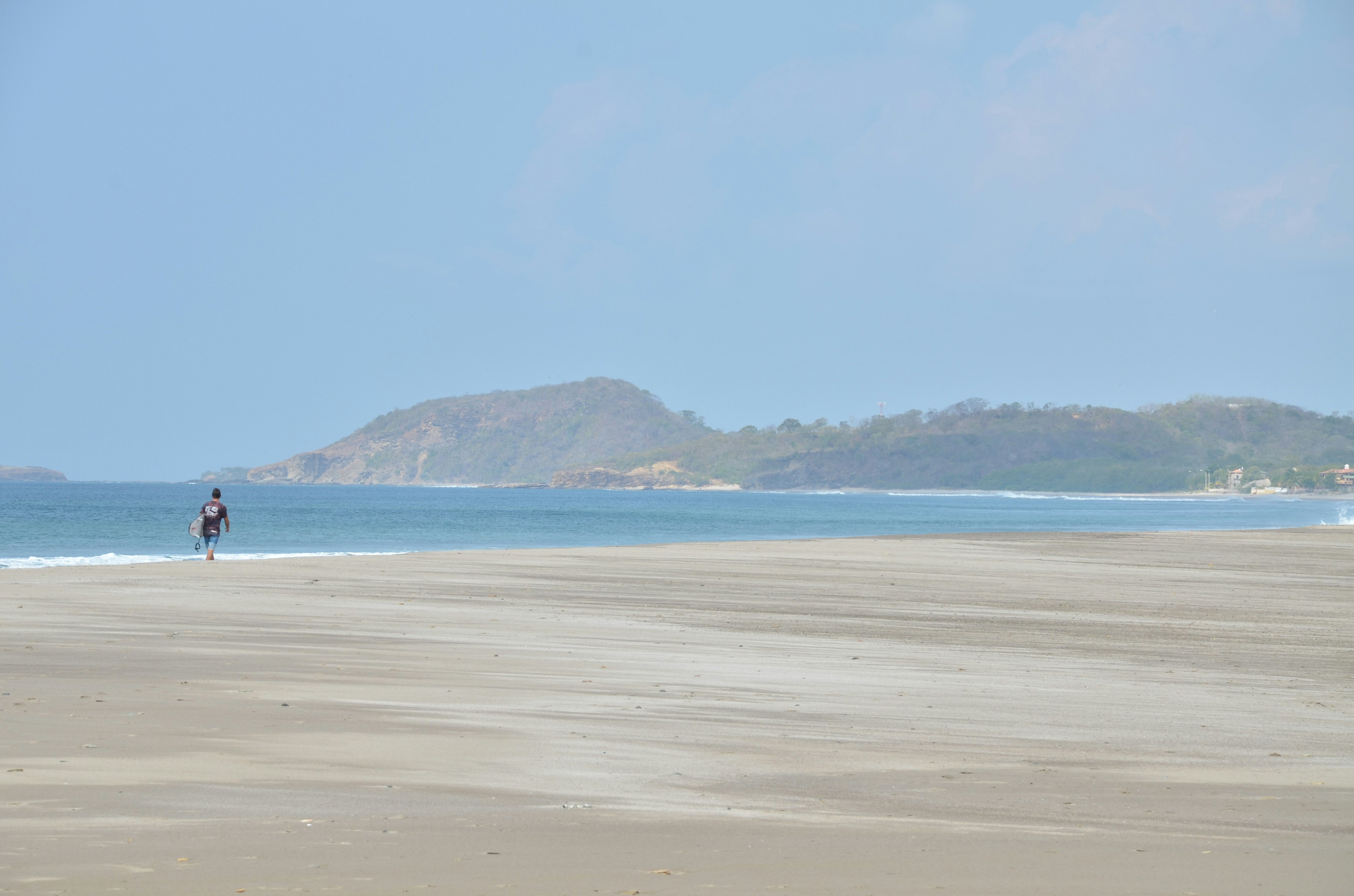 A surfer walks on an expansive beach