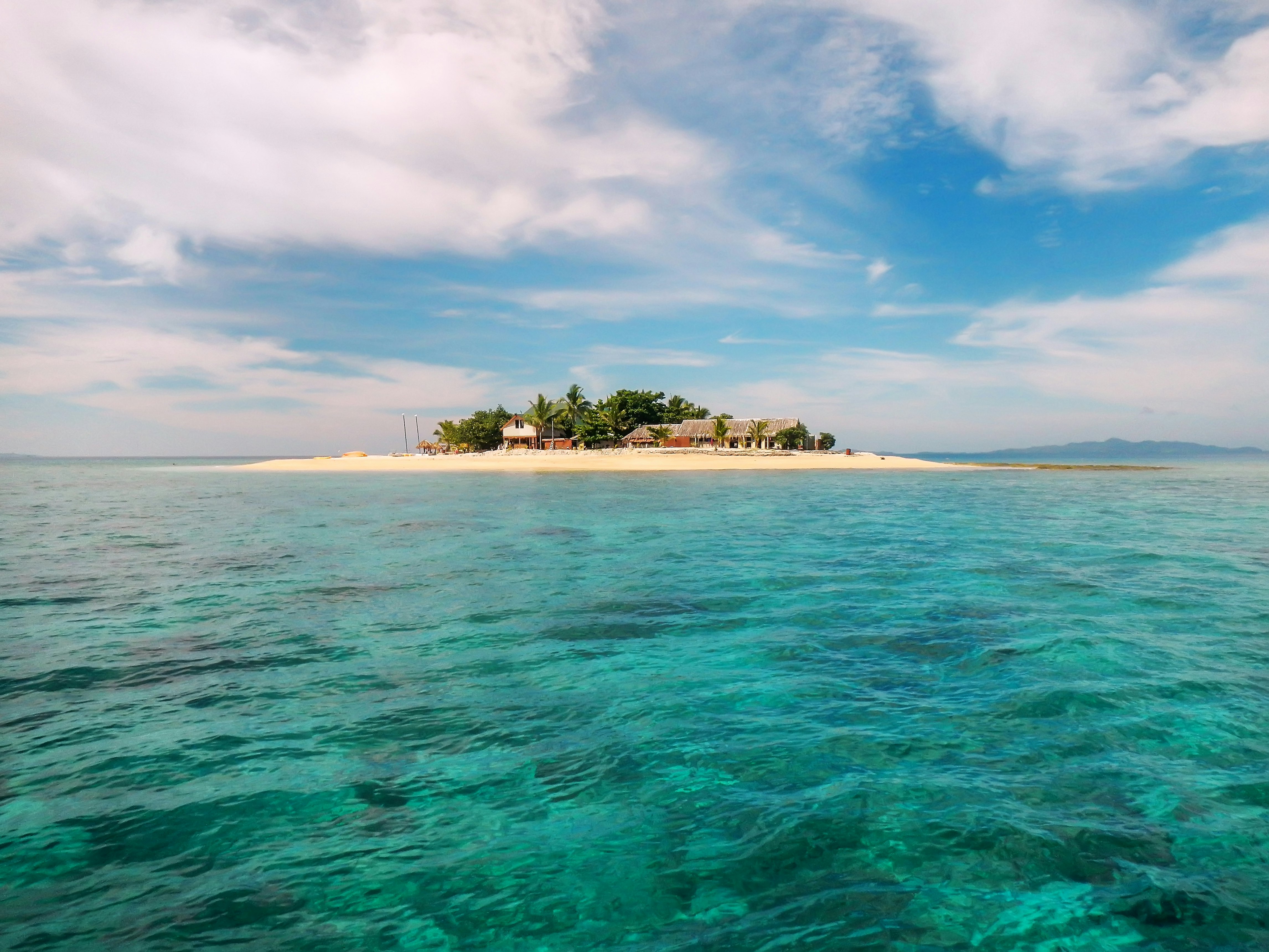 Small huts sit on a picturesque island in the middle of the ocean.