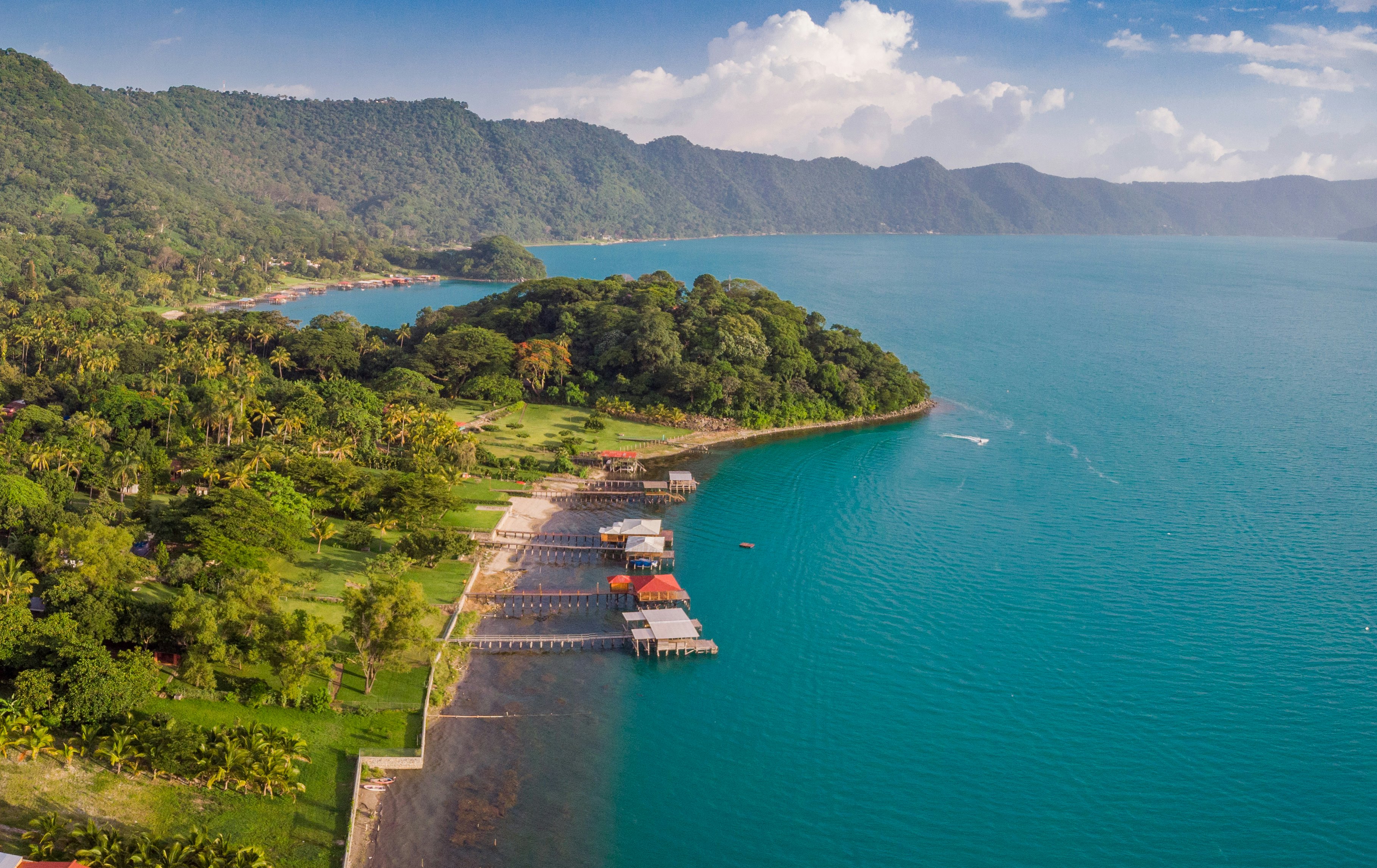 Aerial view of a blue green lake with stilt houses over the water in the foreground.