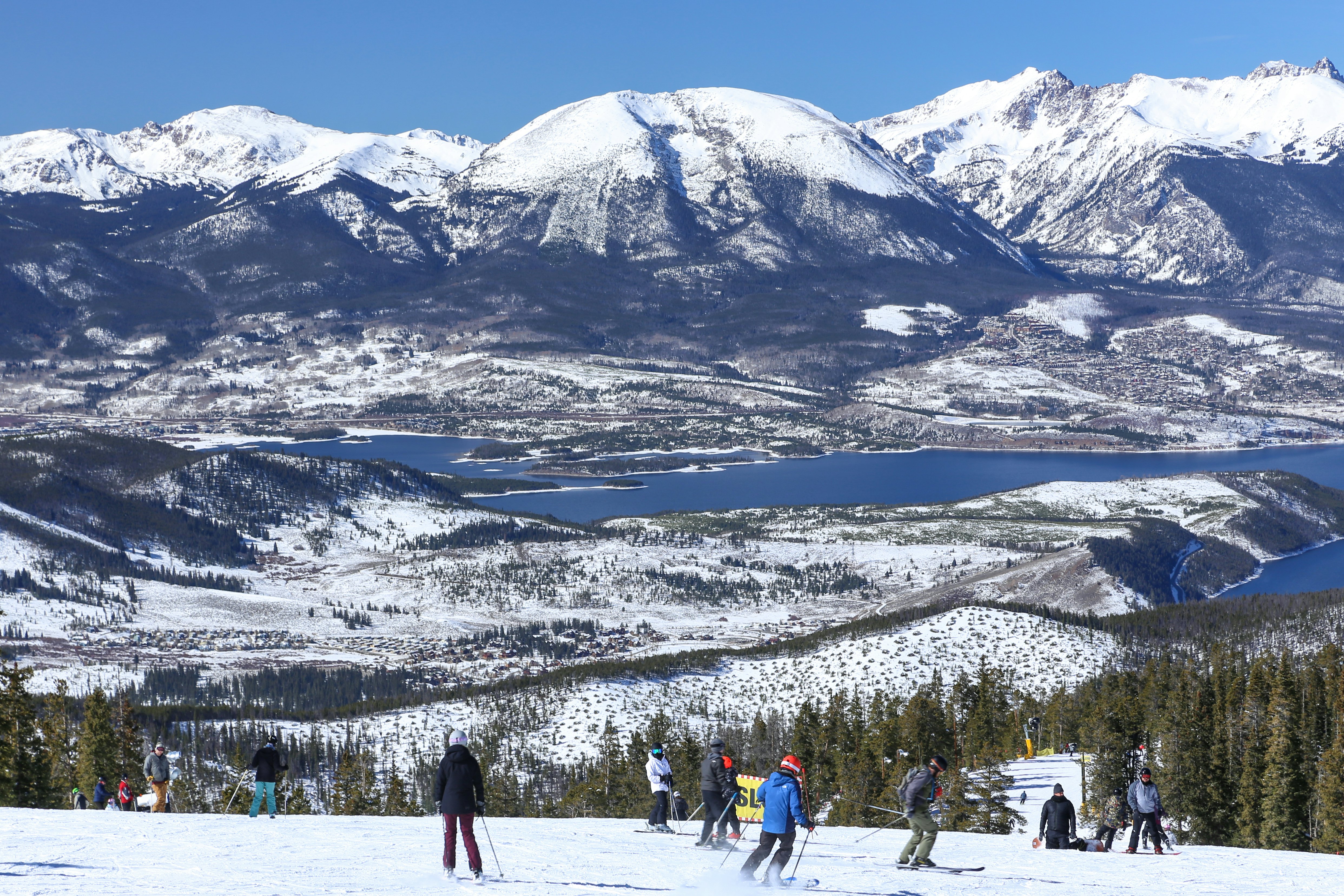 A group of skiers on a mountain above a lake, with more mountains on the other shore.