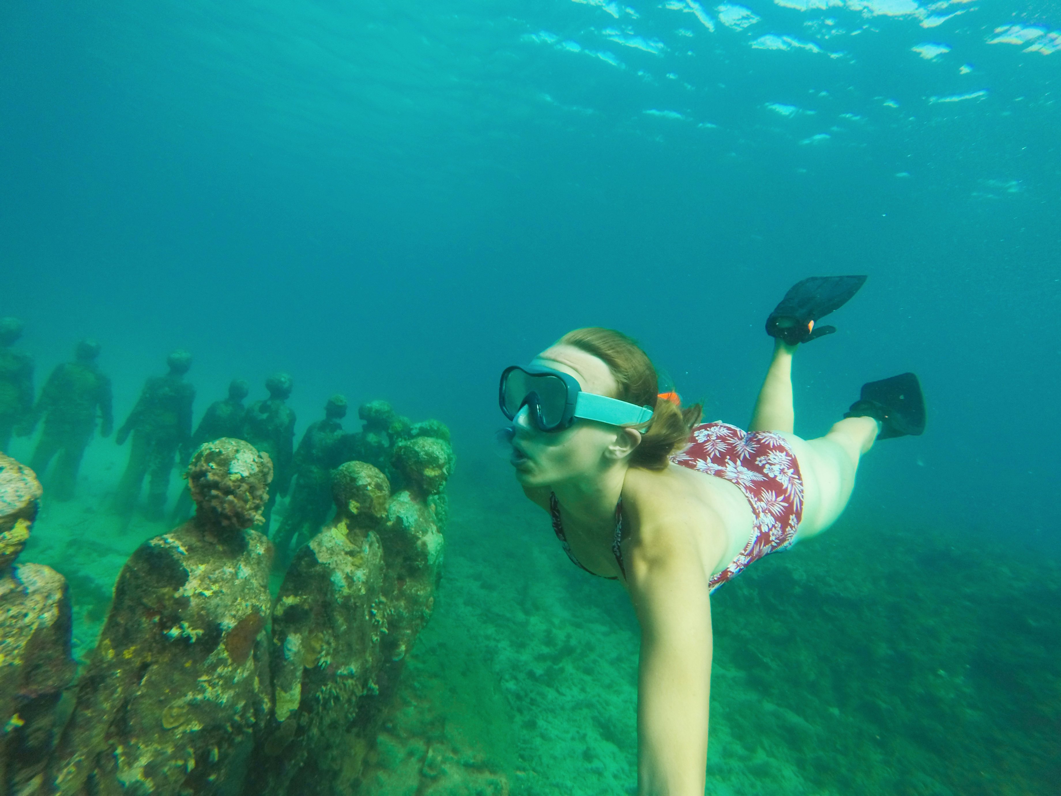 A young girl free diving with goggles and pins while looking at an underwater sculpture