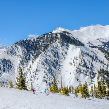 Beautiful view of Rocky Mountains range in Colorado, USA, near Aspen, Colorado, on clear winter day; ski slope with small blurred figures of skiers at the bottom of the range; blue sky in background, License Type: media, Download Time: 2025-08-28T14:27:33.000Z, User: catalinaaragon, Editorial: false, purchase_order: 56530 - Guidebooks, job: Global Publishing WIP, client: Western USA 7, other: CA