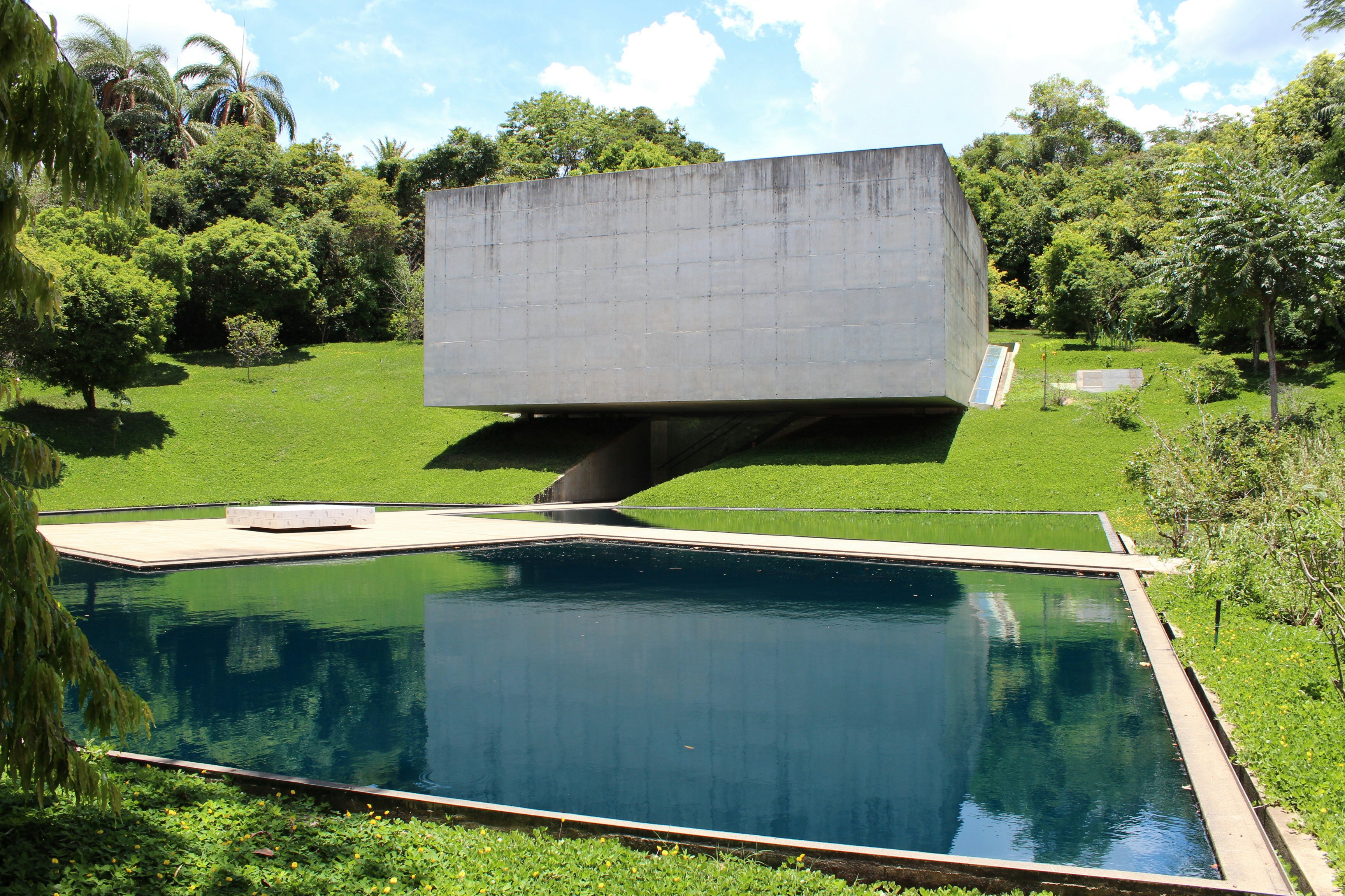 A concrete building inserted on the grass "floats" above a blue pool.