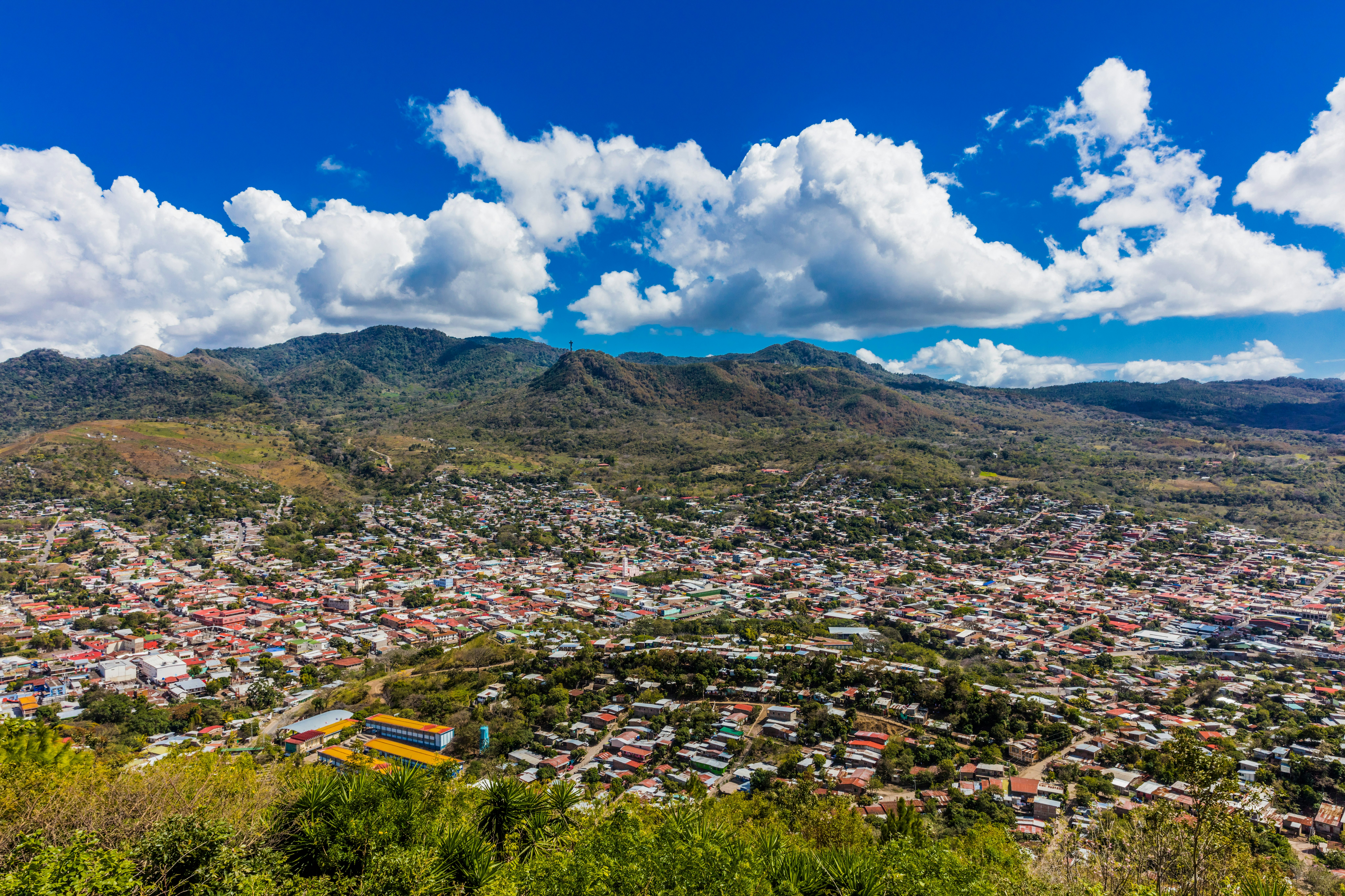 A densely packed city in a valley below green rolling hills.