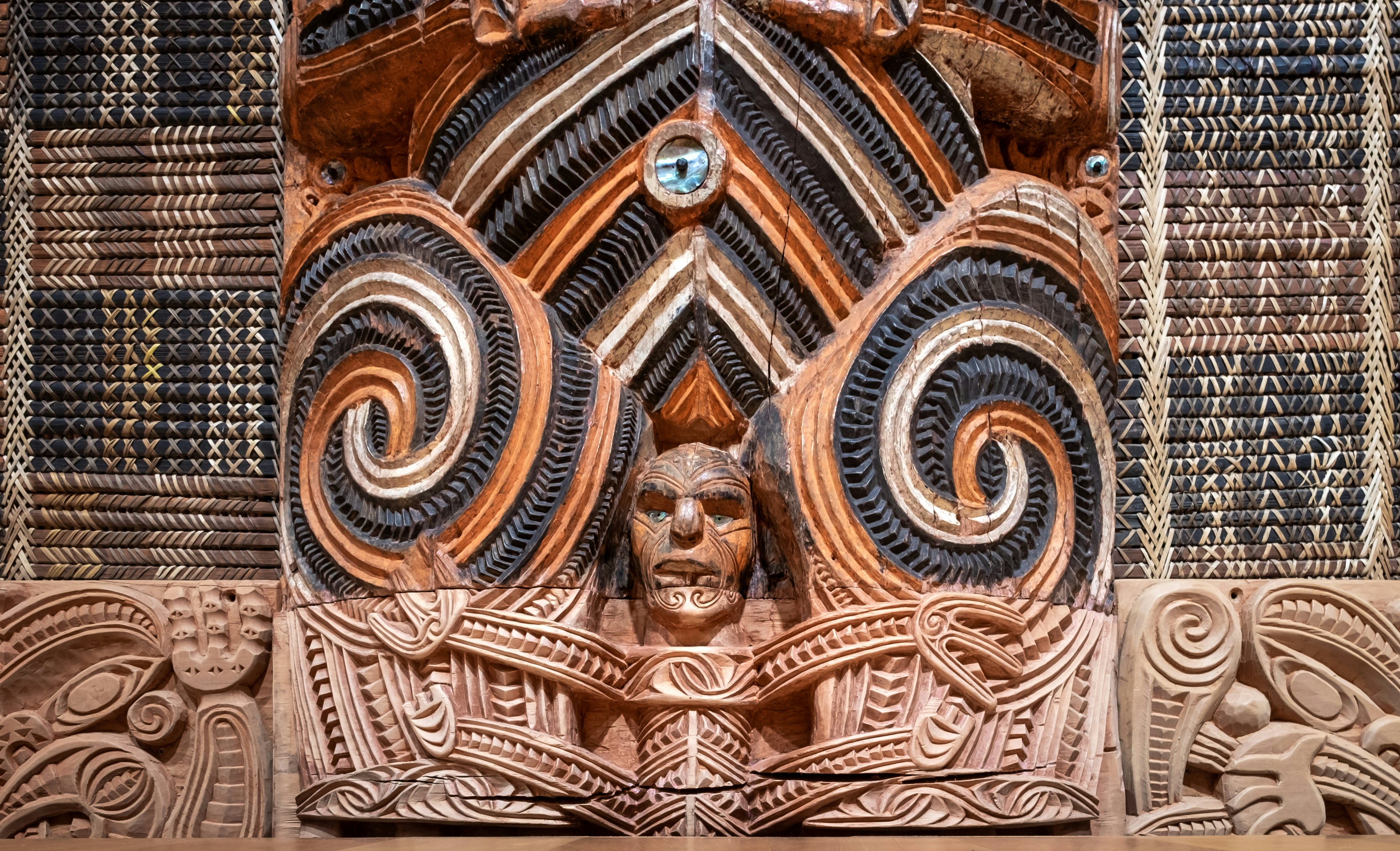 A detail of an intricate Māori carving, with a face at the center and elaborate designs around it.