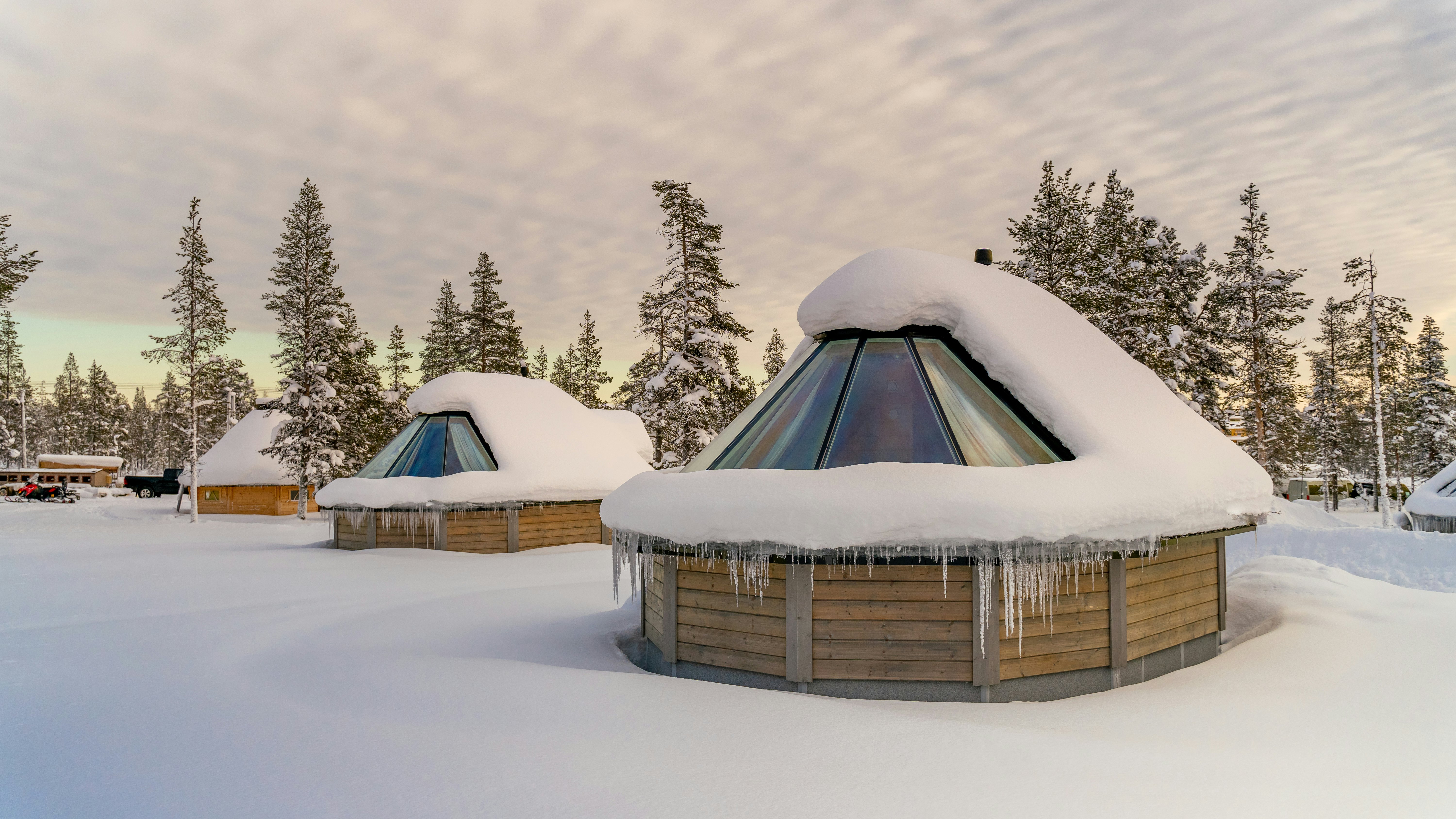Igloo-shaped buildings with glass roofs in Finland; snow blankets the ground, partially covering the domed roofs, and is dusted on evergreen trees.