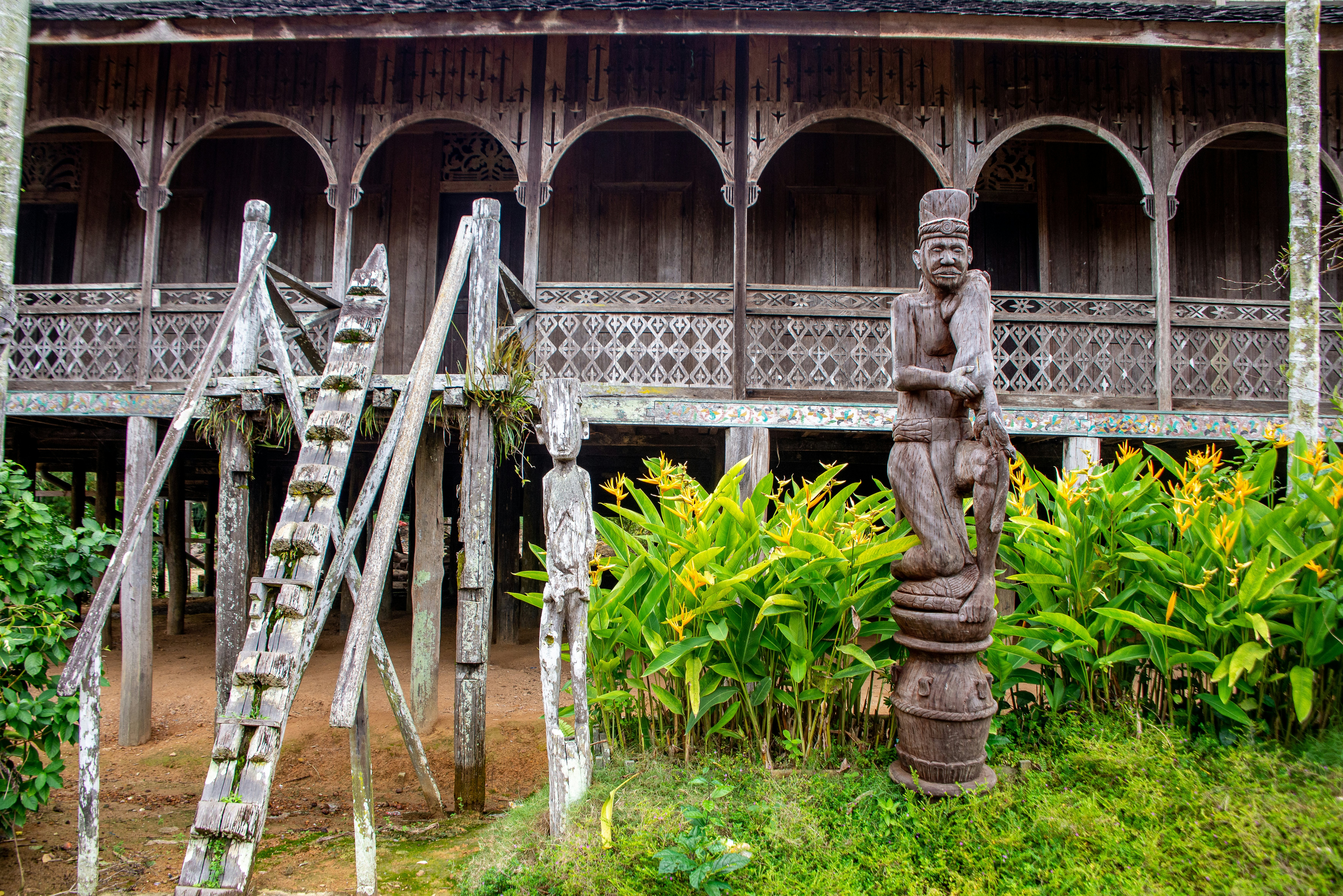 Carved wooden sculptures sit outside a wooden structure with a carved facade.