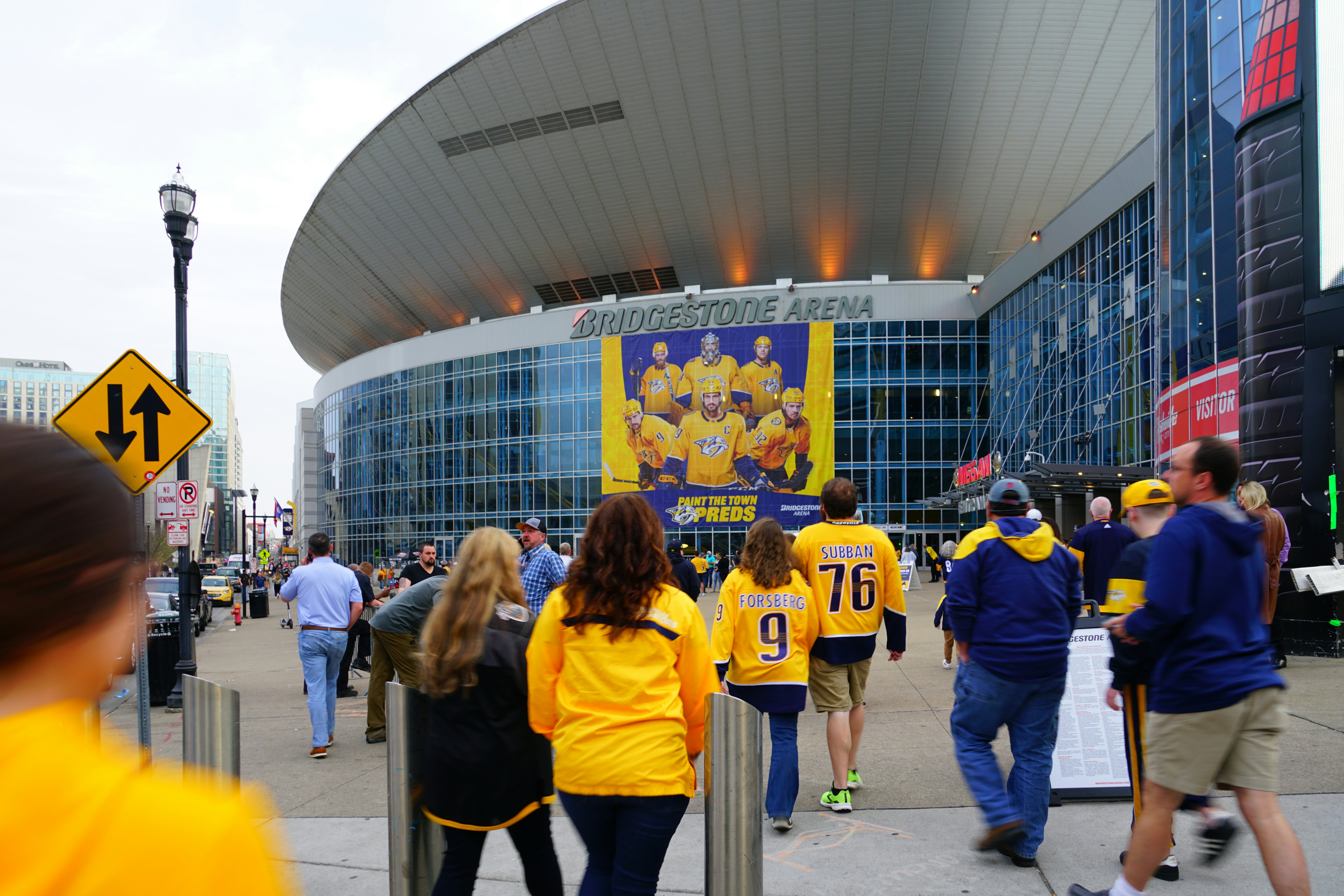 Sports fans walking into a rounded glass building with the words "Bridgestone Arena" on the front.