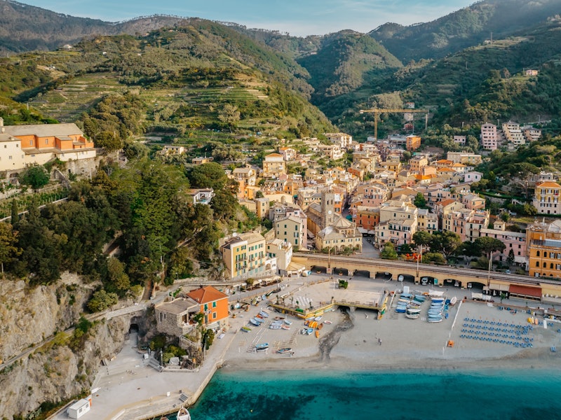 Aerial view of a classic clifftop town with colorful buildings, vinetards and field overlooking a beach and port