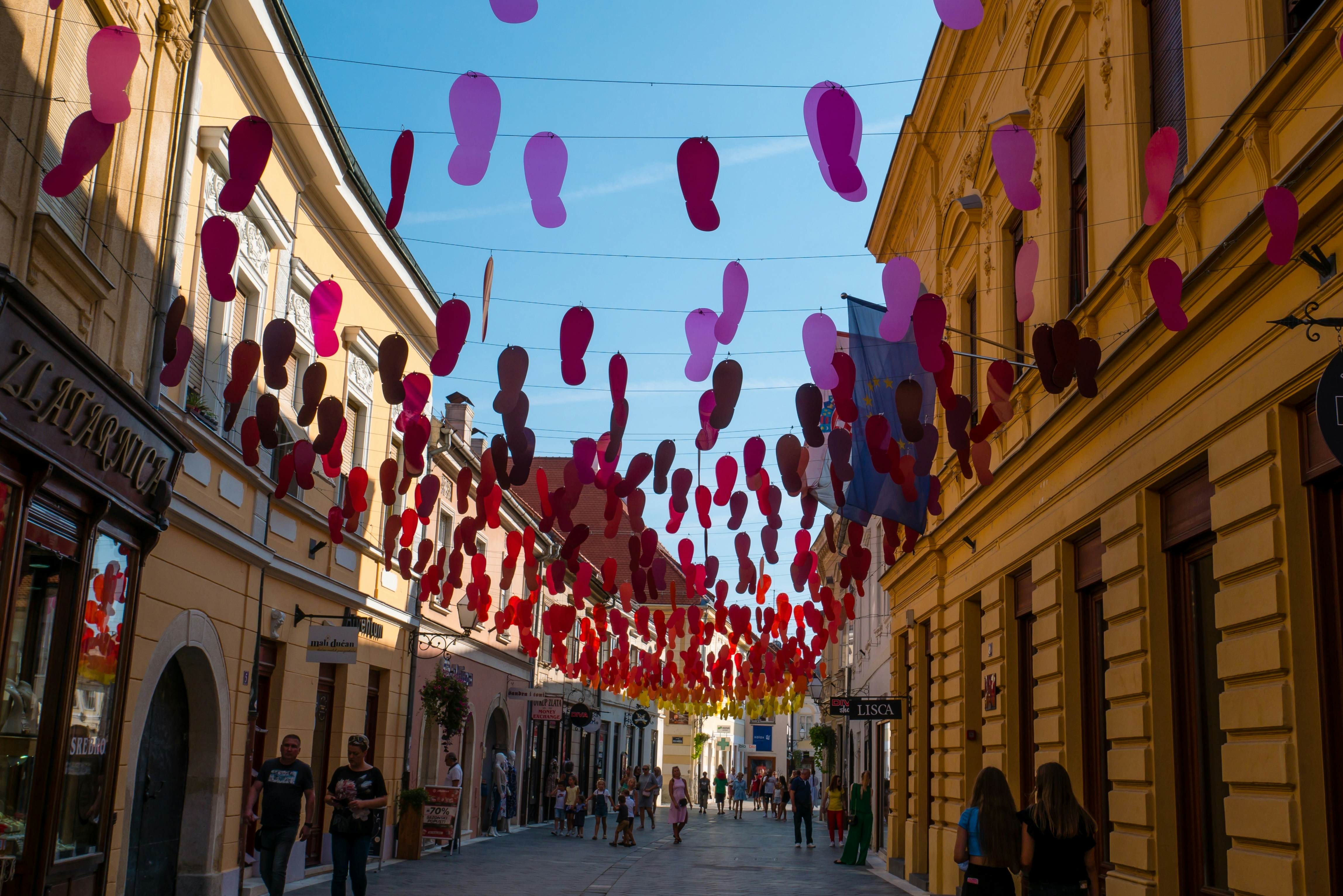 Footstep shapes in purple and red hang from wires strung over a pedestrian street in Varaždin, Croatia.