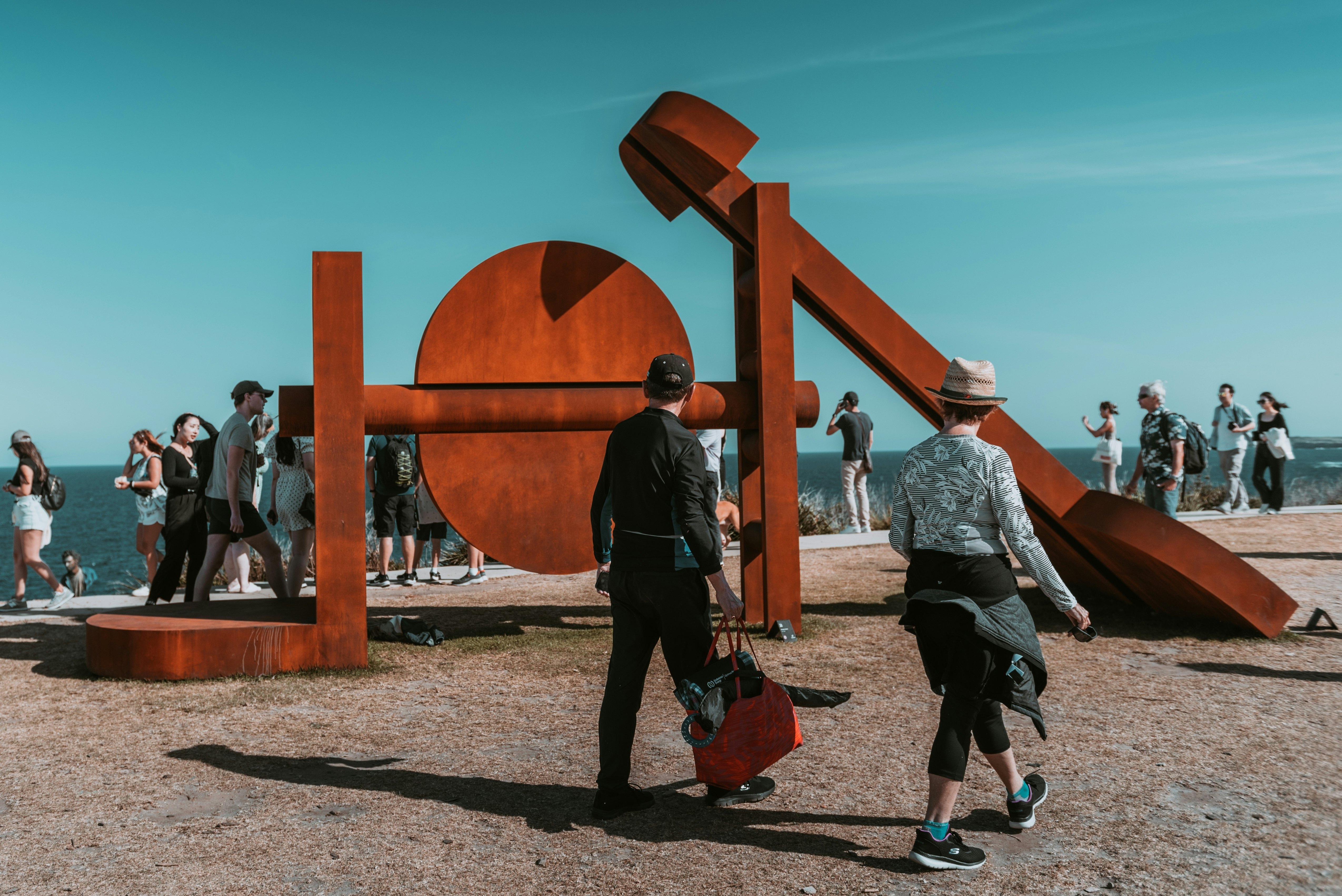 Two people walk by a big rust-colored sculpture