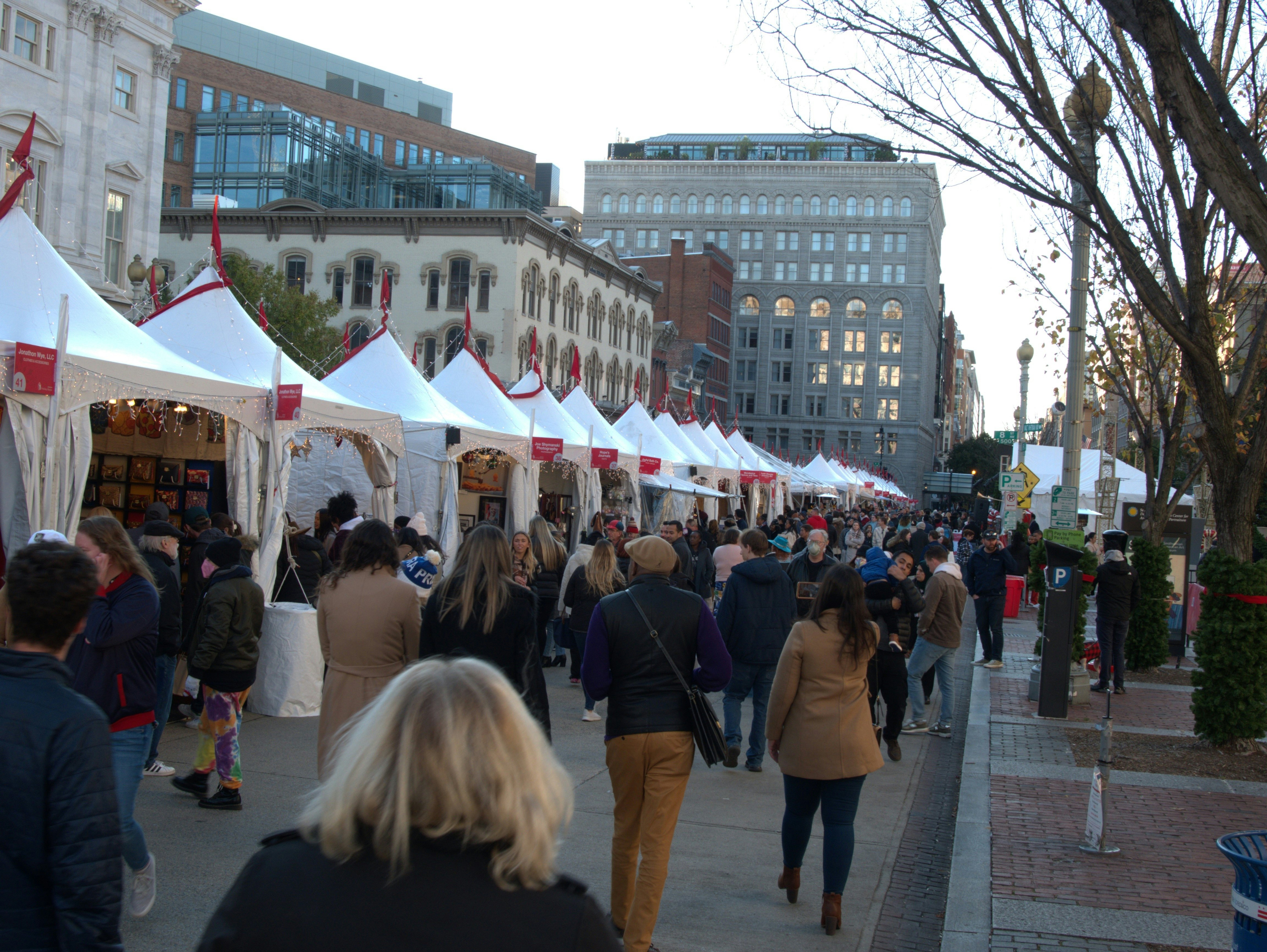 People walking by white-tented booths in a city's open-air market