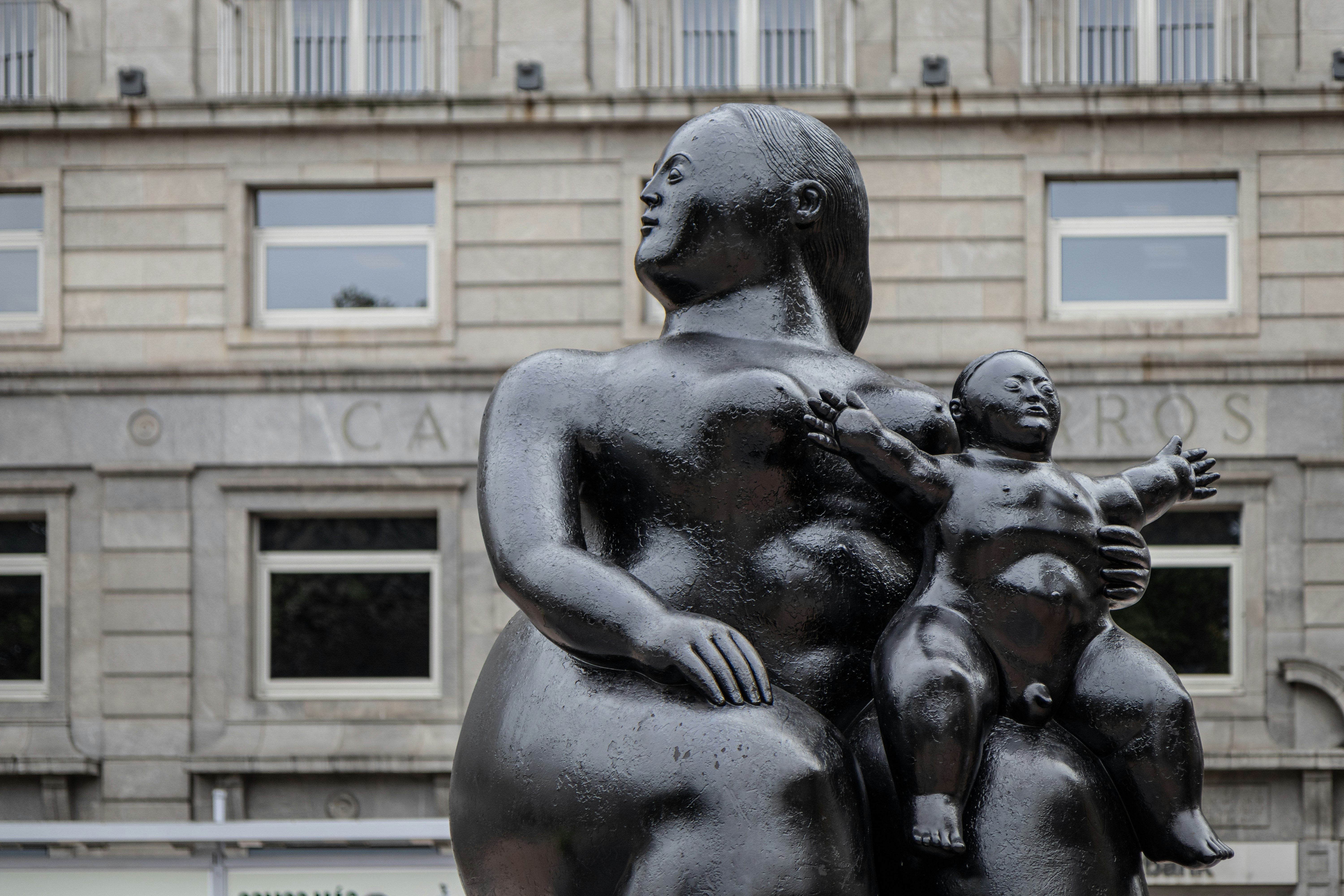 OVIEDO, SPAIN-AUGUST 10, 2021: Close up of La Maternidad sculpture (Sculptor: Fernando Botero) with an historic building in the background.