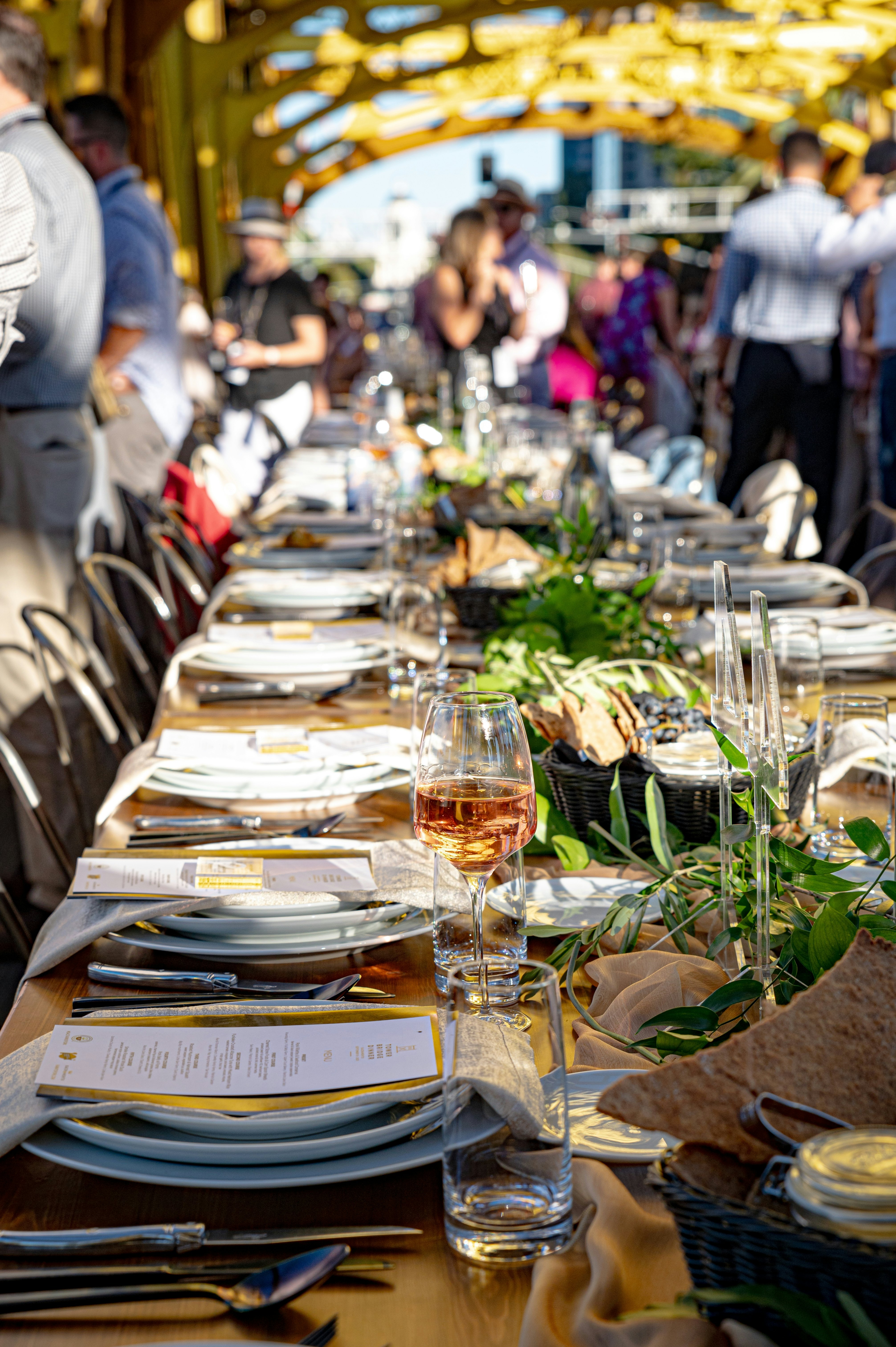 A long open-air dining table set for a meal, with many diners milling around in the background.
