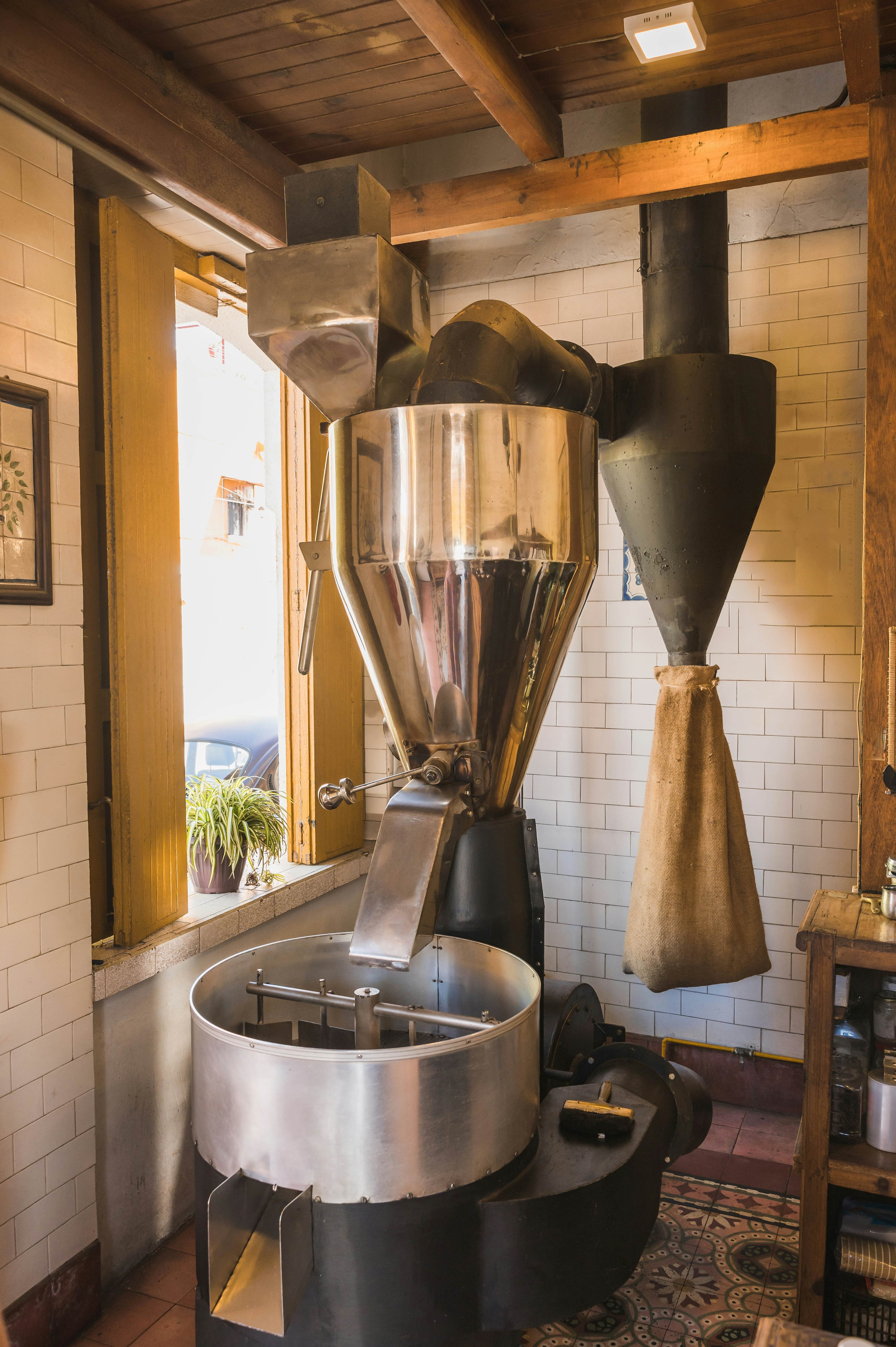 A large coffee grinder inside a building with a burlap coffee bag hanging in the background.