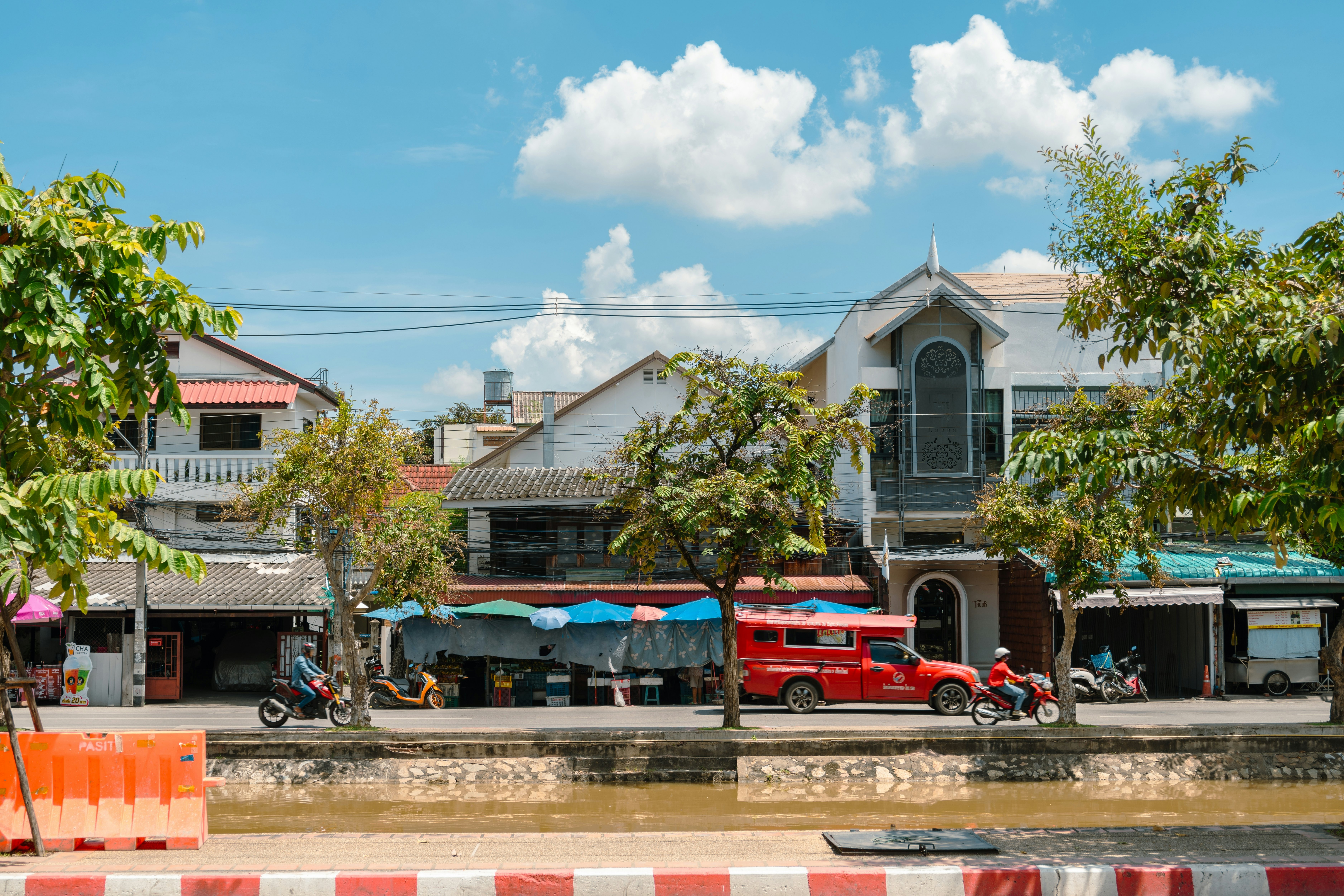 Two motorcyclists and a red truck on a canalside street.