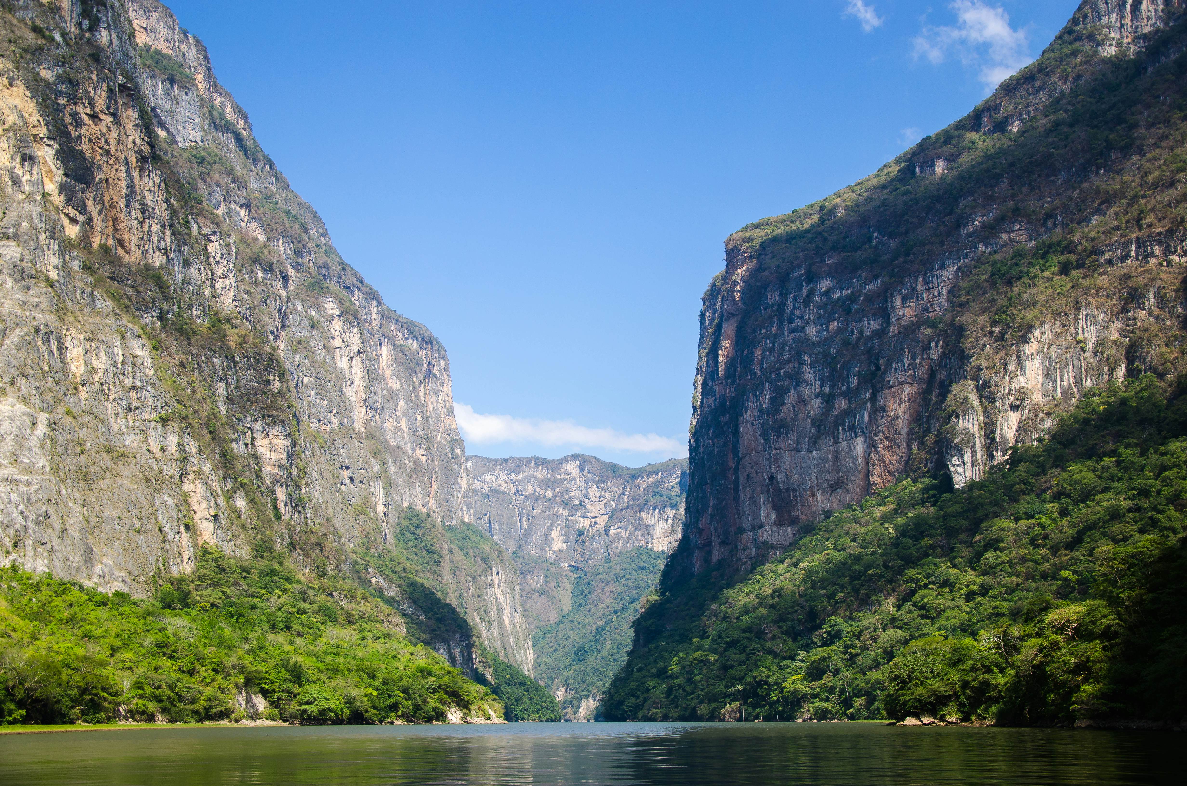 A body of water in a canyon surrounded by tall, rocky mountains on a sunny day.