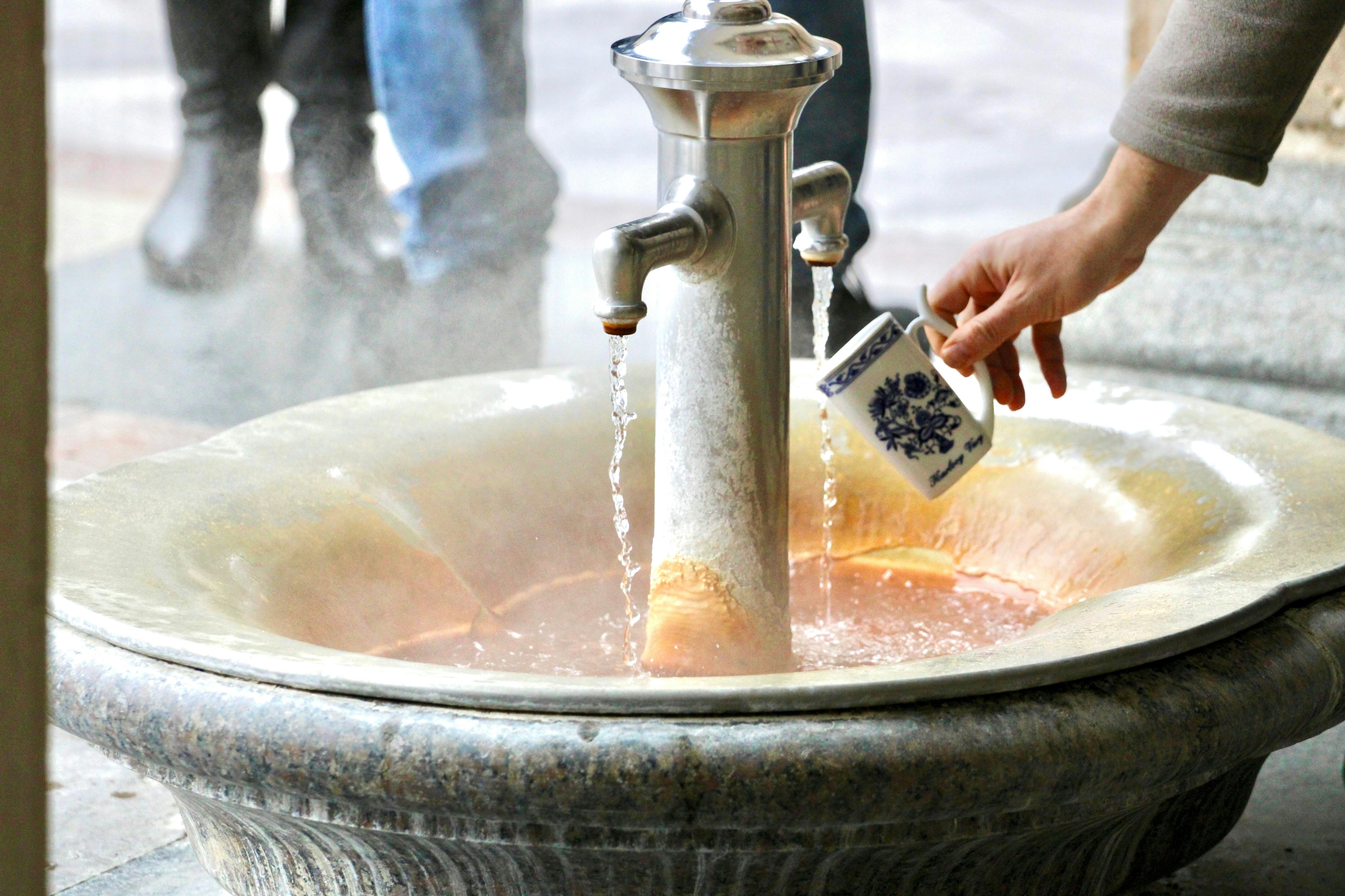 Hot mineral water source in the building The Mill Colonnade in Karlovy Vary, Czech Republic. Catching a water from hot mineral spring in Karlovy Vary, special mug.