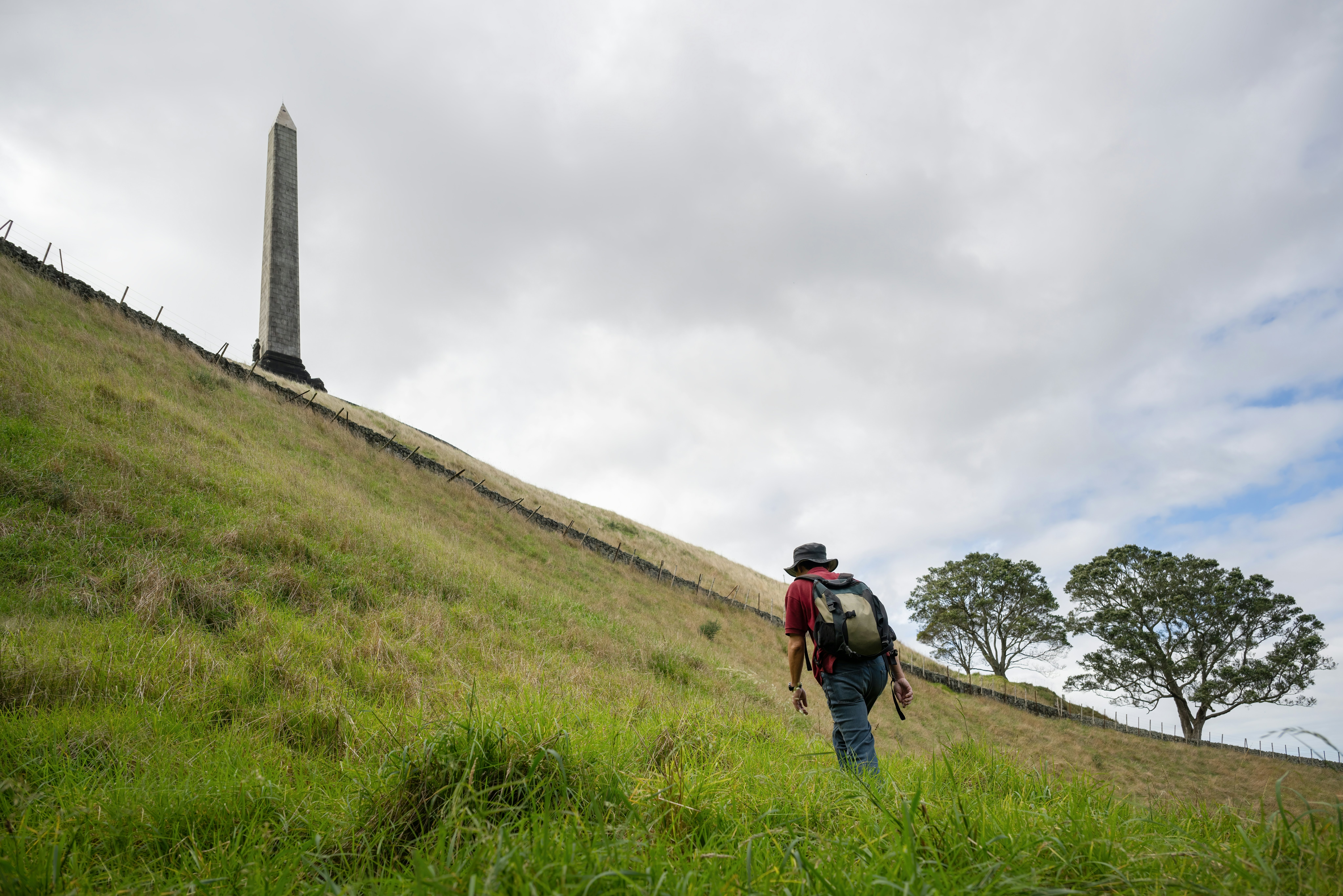 Man walking uphill towards the Obelisk on top of One Tree Hill. Auckland.