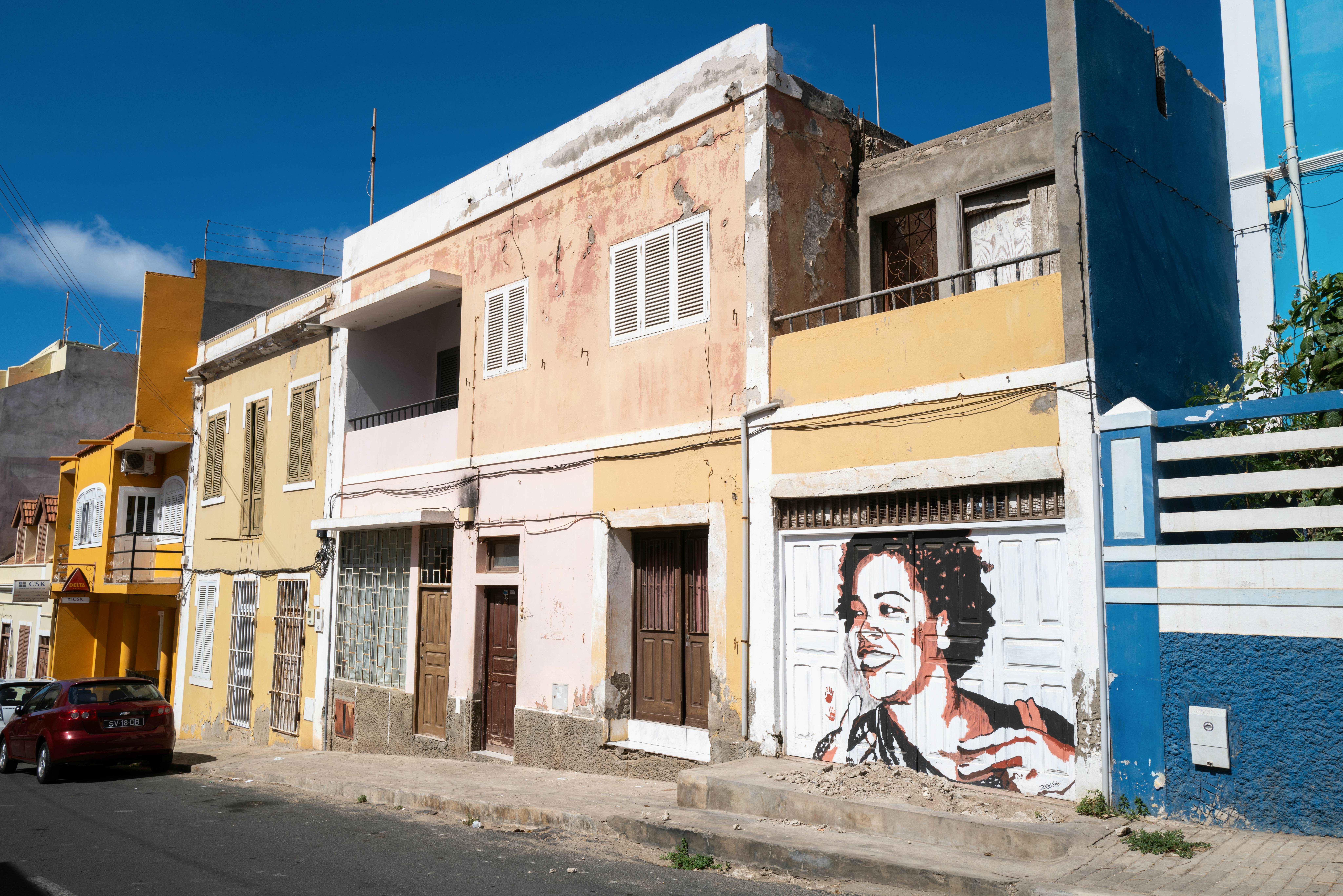 A row of buildings in a street in a town, with a painted mural depicting a smiling woman.