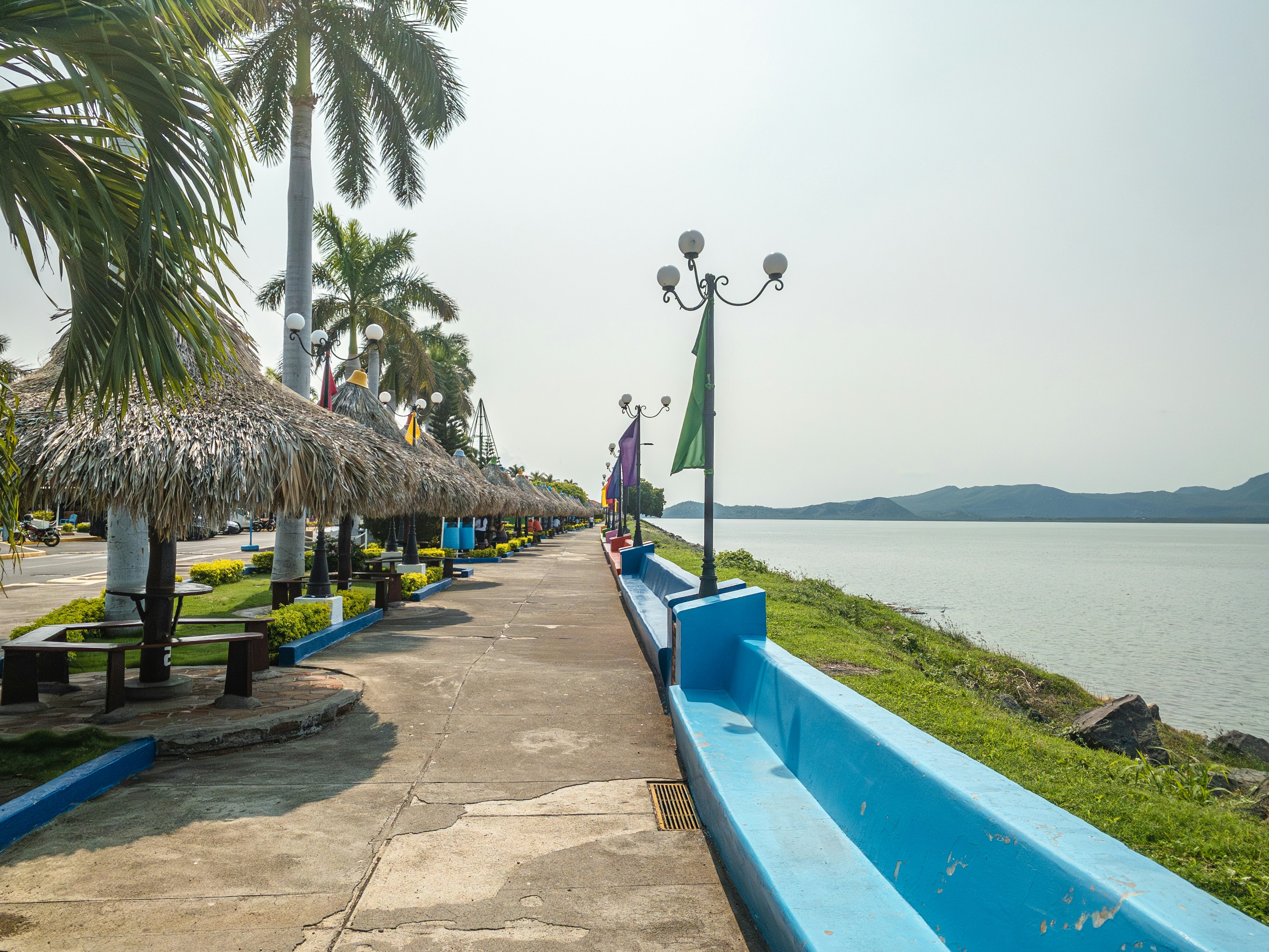 A waterfront promenade lined with flags and palm trees.