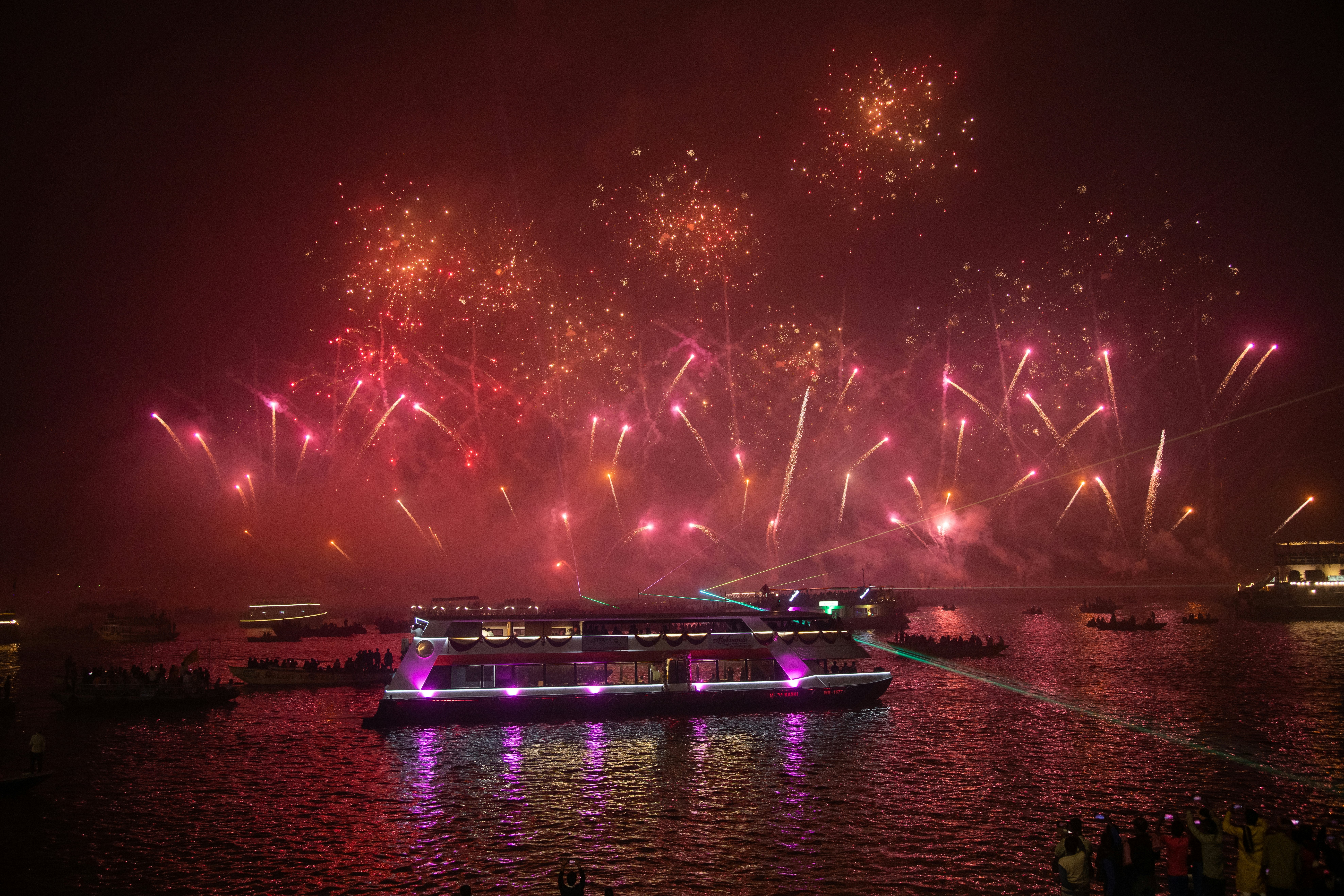 Red-tinted fireworks explode over boats in a river.