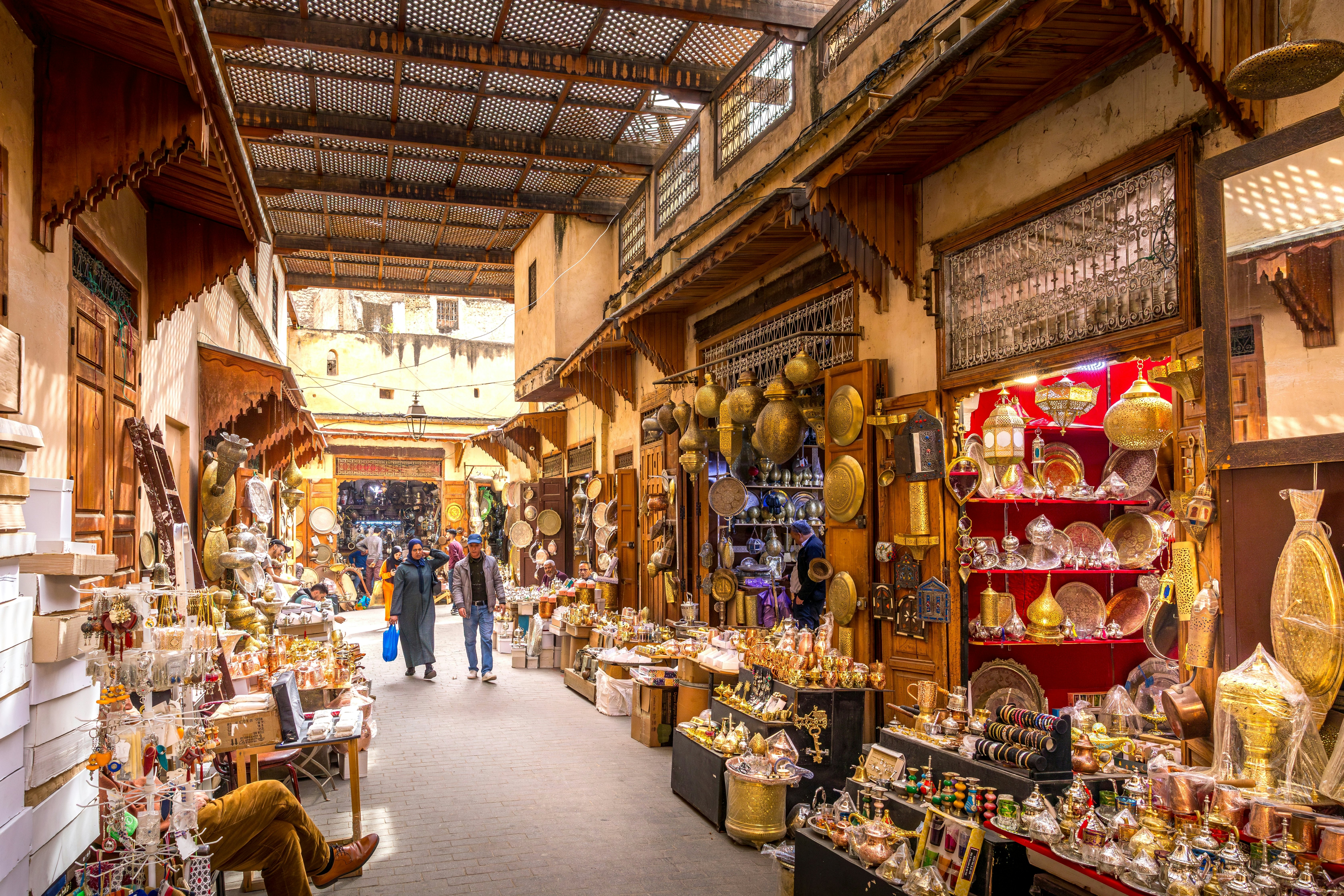 Two shoppers stroll down a narrow street lined with stalls selling gifts and souvenirs of local crafts.