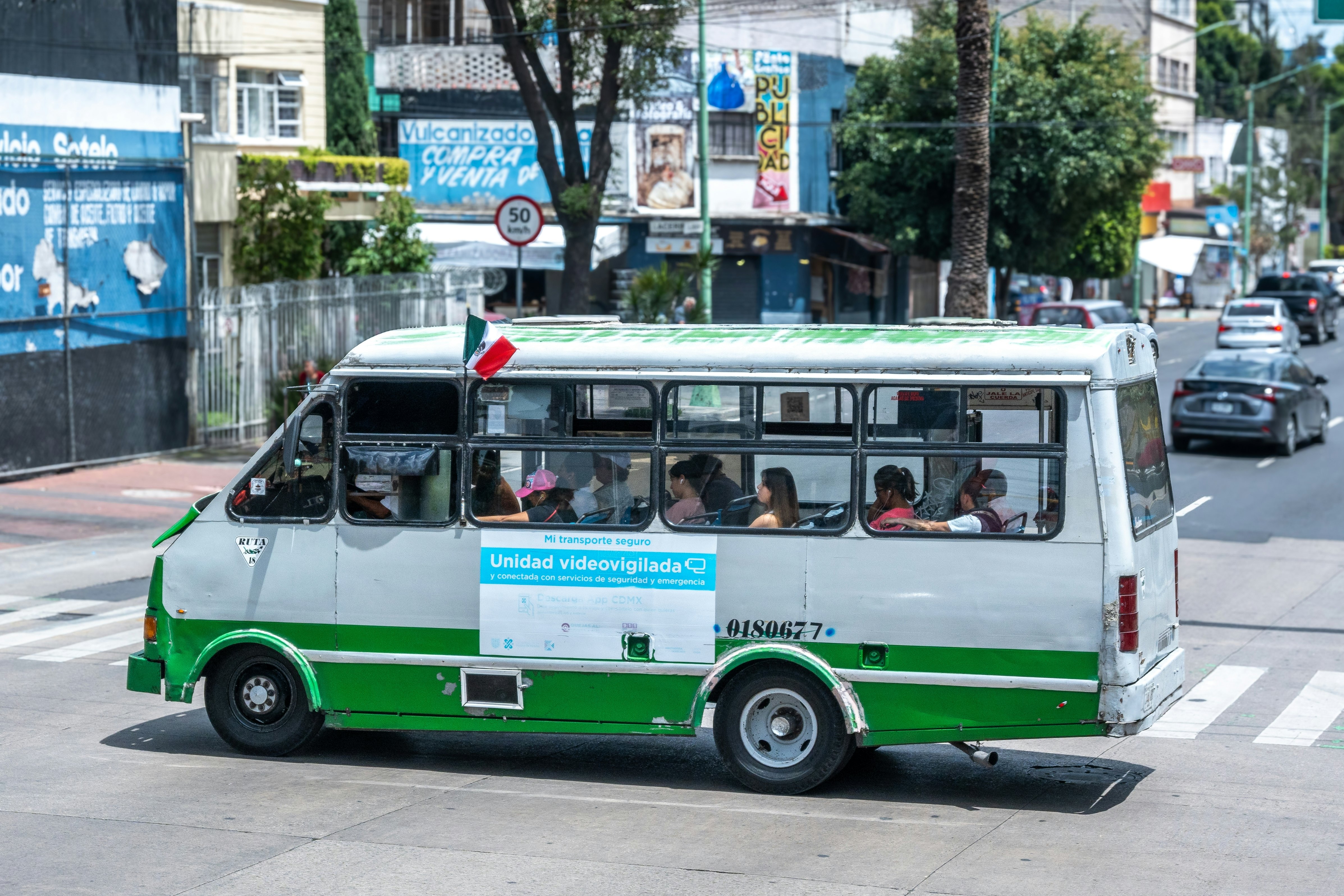 A minibus holding passengers and displaying a flag drives in a city street.