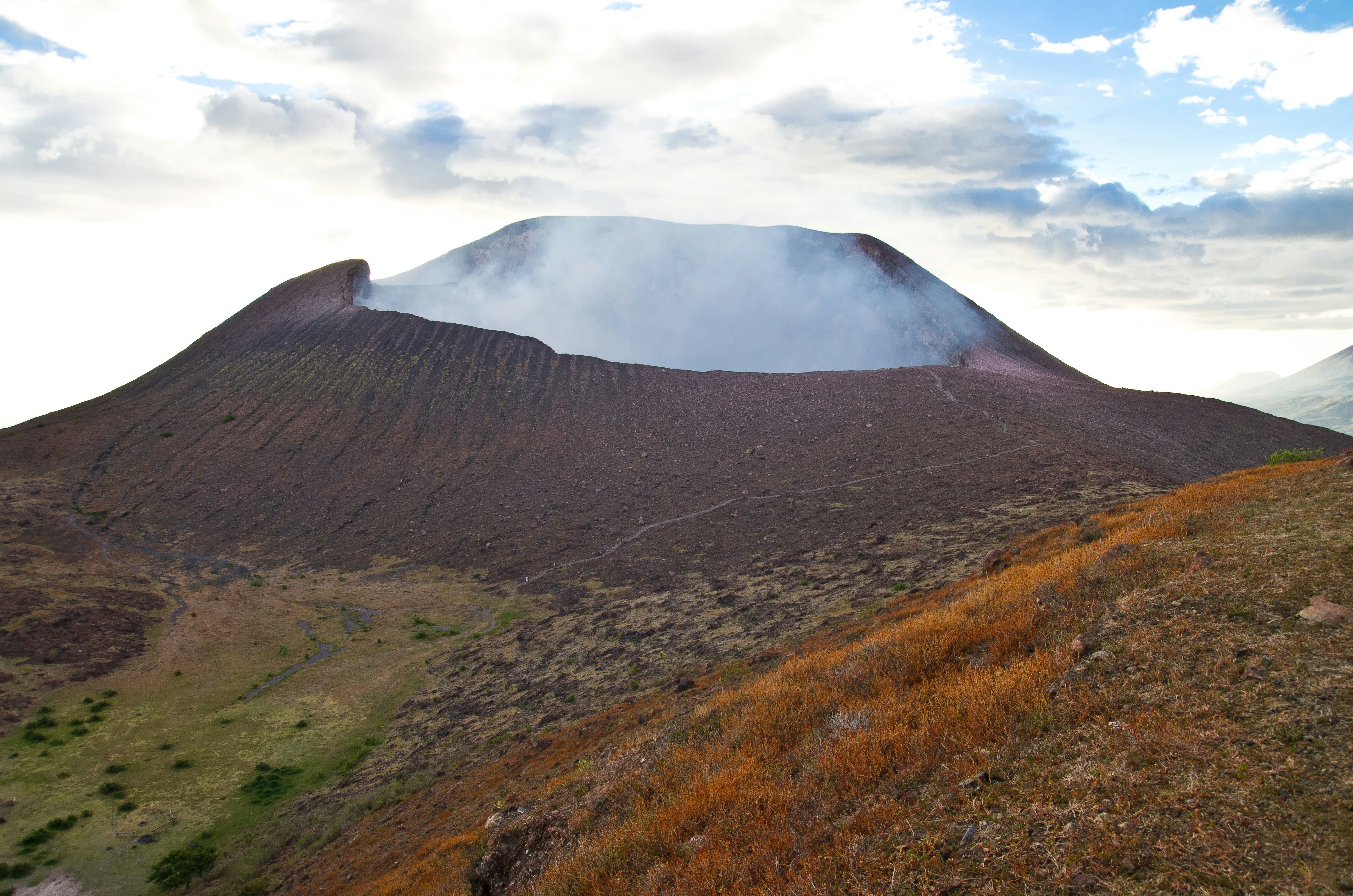 A red dusty landscape on the slopes of a smoking volcano crater.