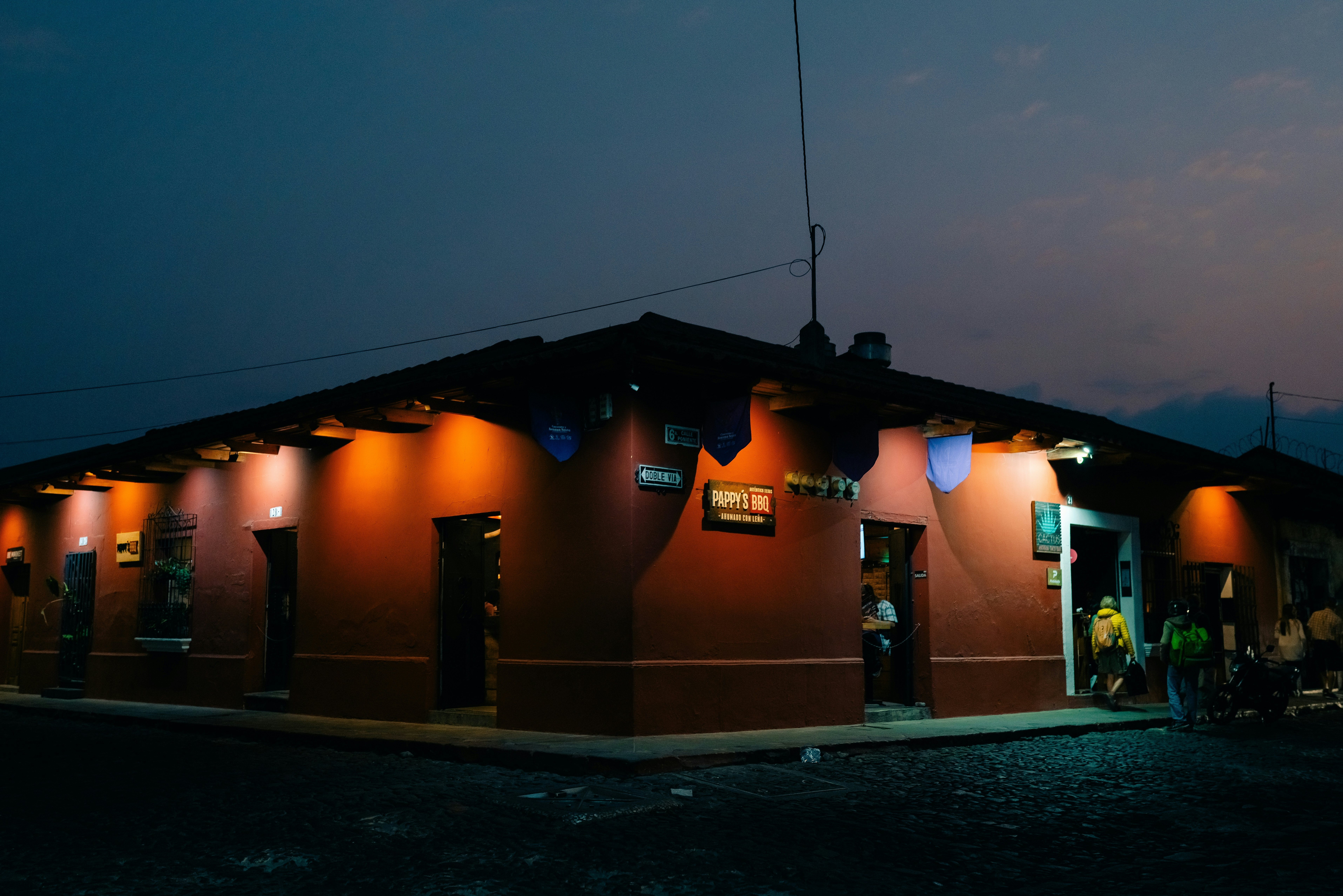 A restaurant on a corner at nighttime with people walking outside.