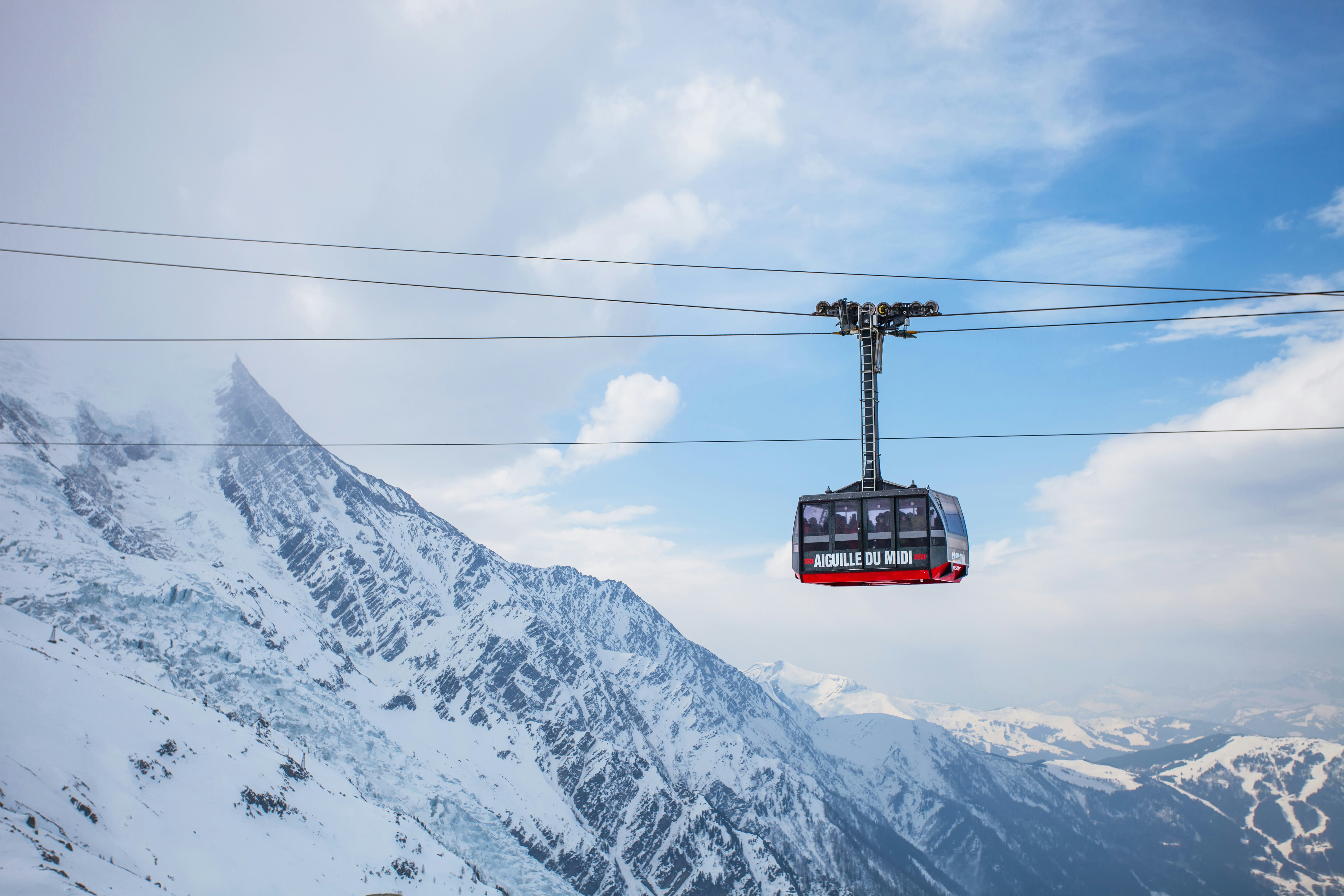 A large gondola travels on cables over snowy mountain slopes.
