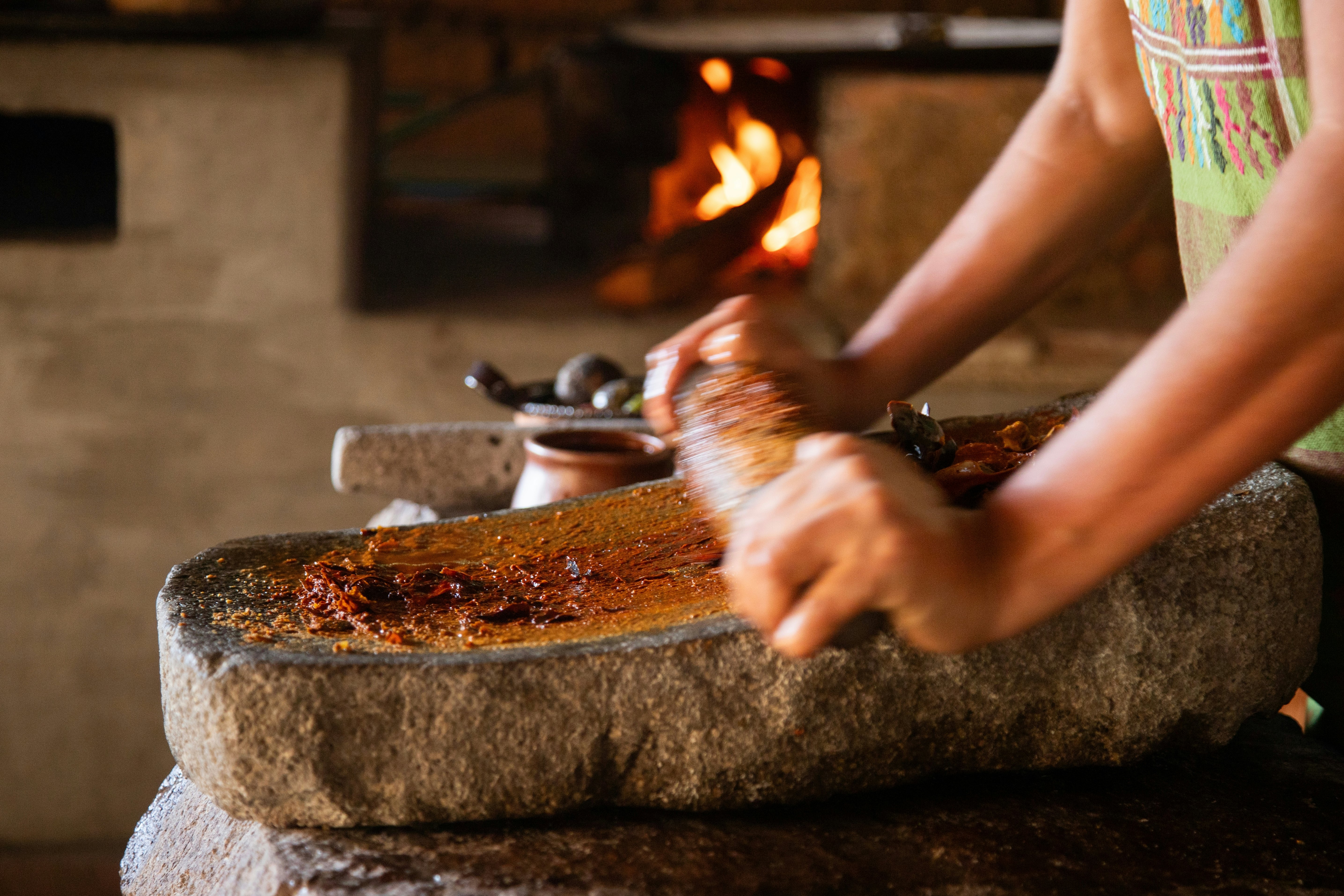 Woman from an indigenous community in Oaxaca preparing traditional red mole with a metate, a tool for grinding ingredients in Mexico.