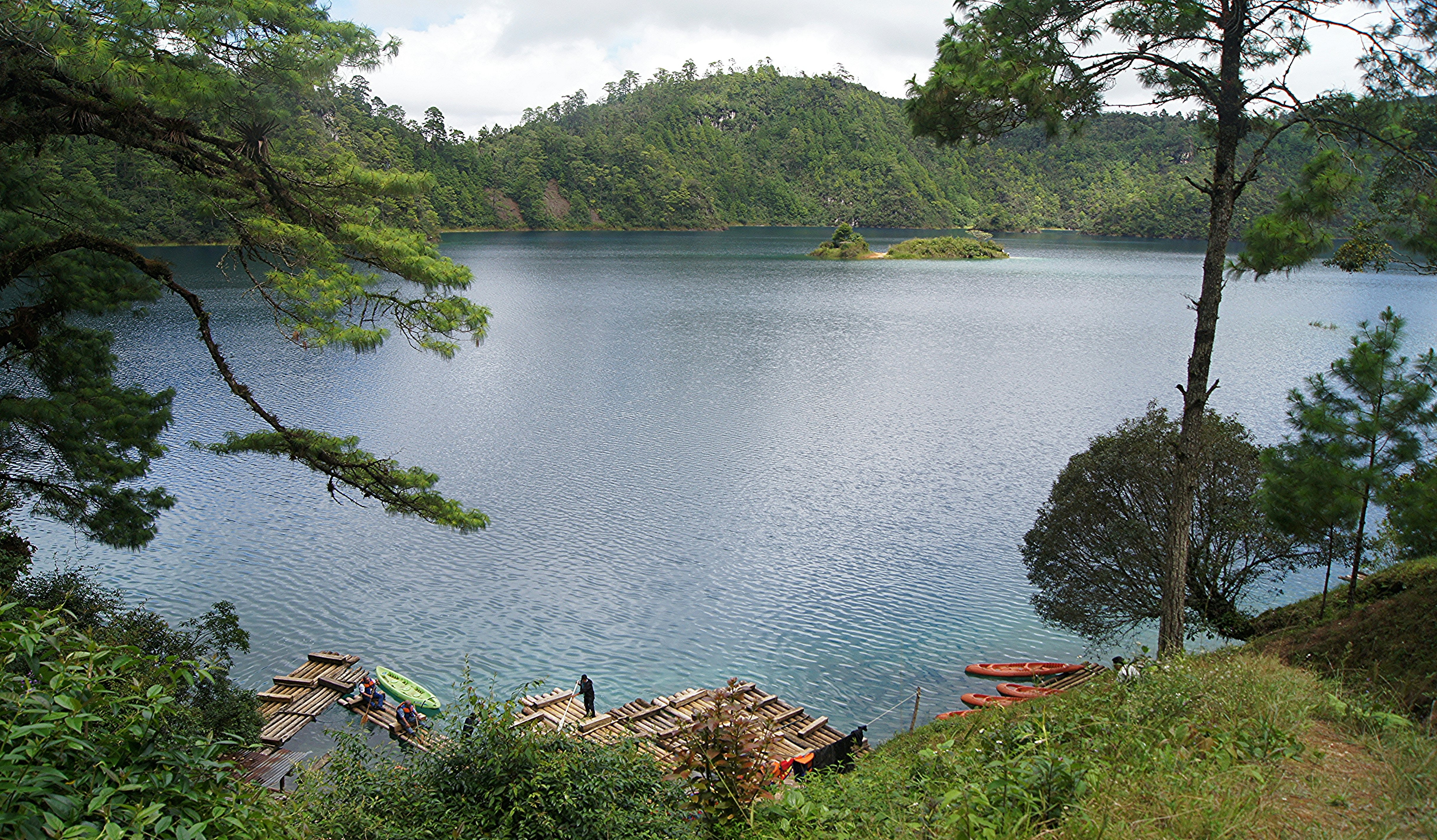Aerial view of lake surrounded by trees and forested hills with docks and kayaks in the foreground.