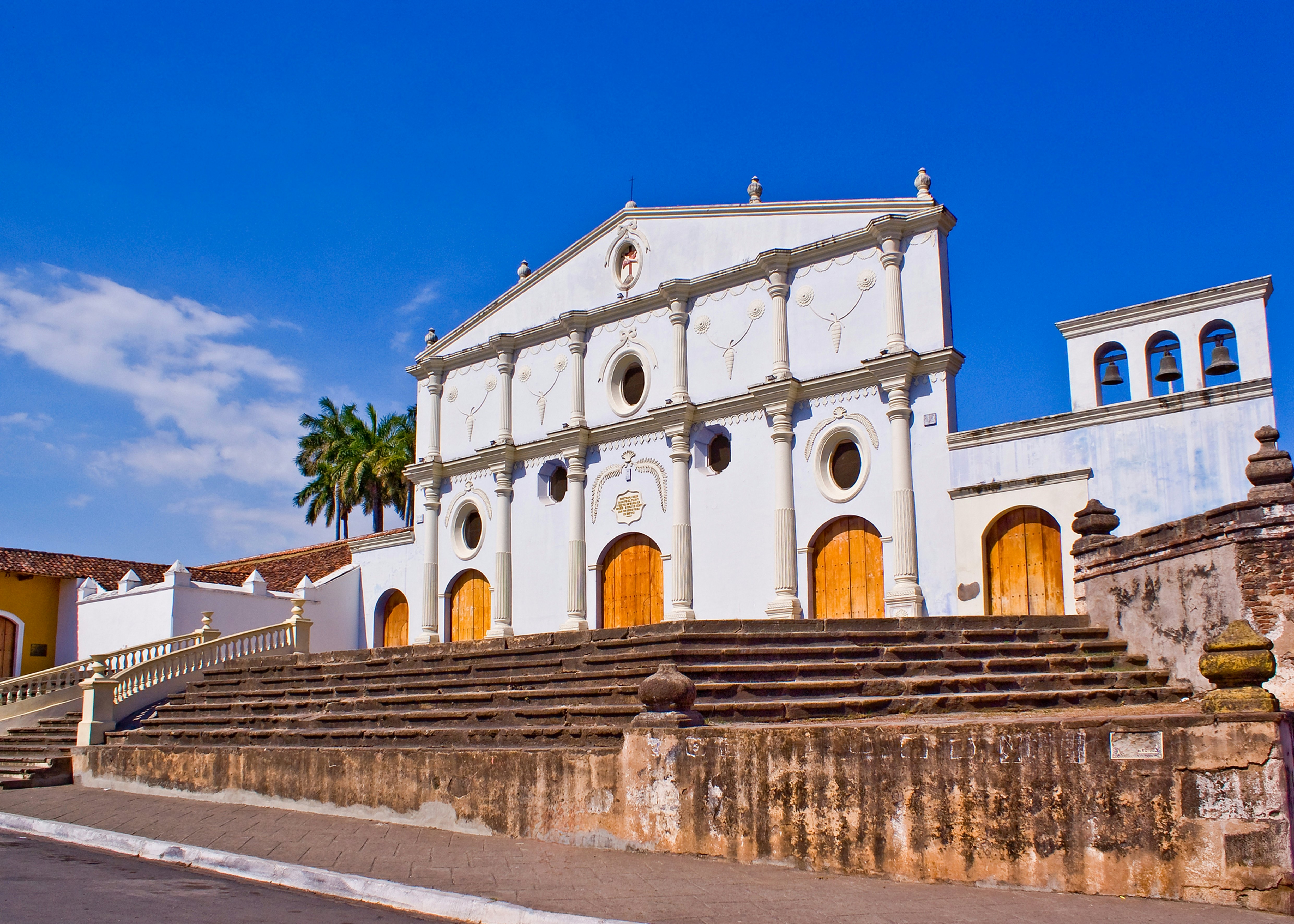 The white facade of an old convent building with three bells in arches.
