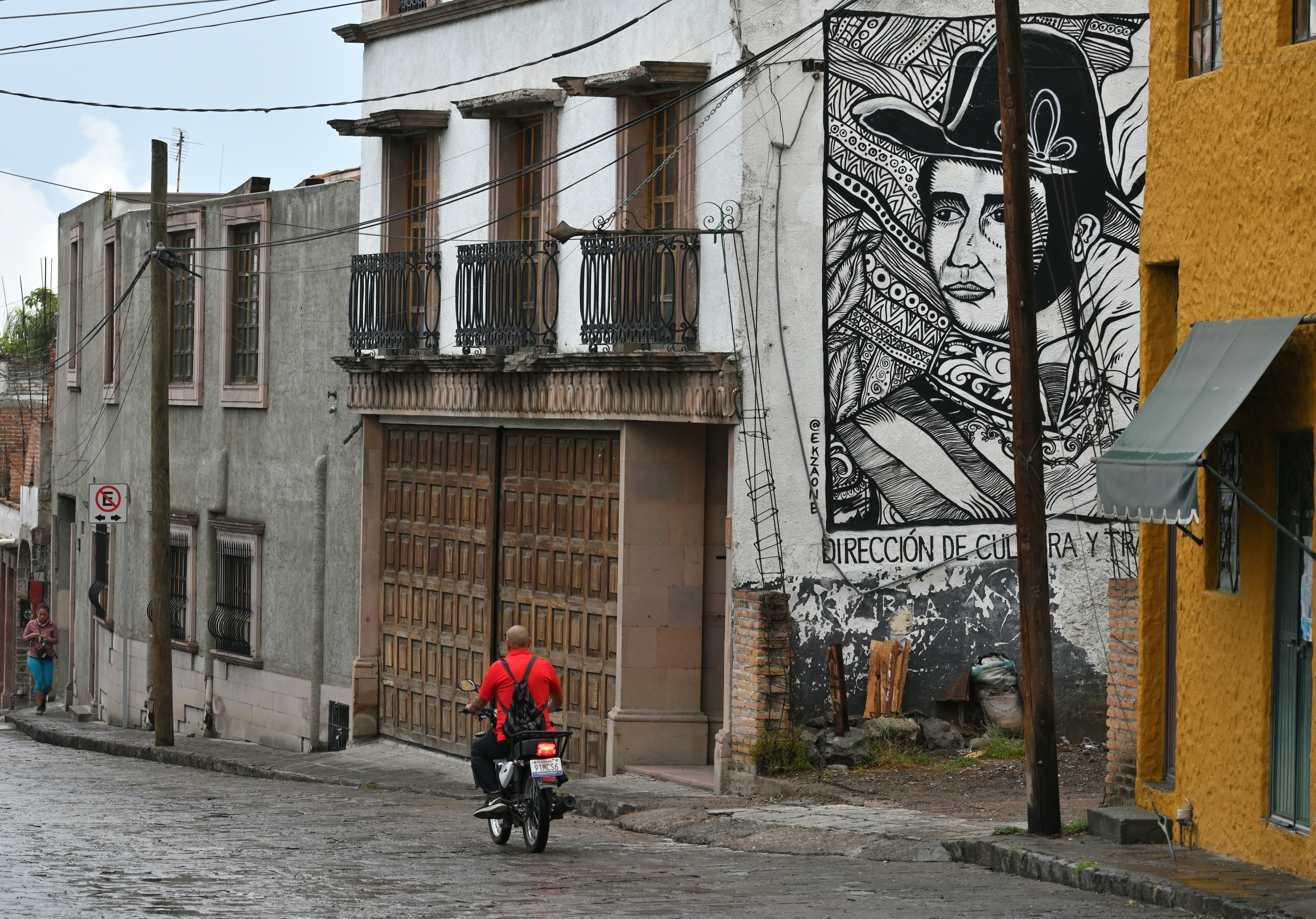 A man rides a motorbike past a large mural painted on the side of a building in a historic city.
