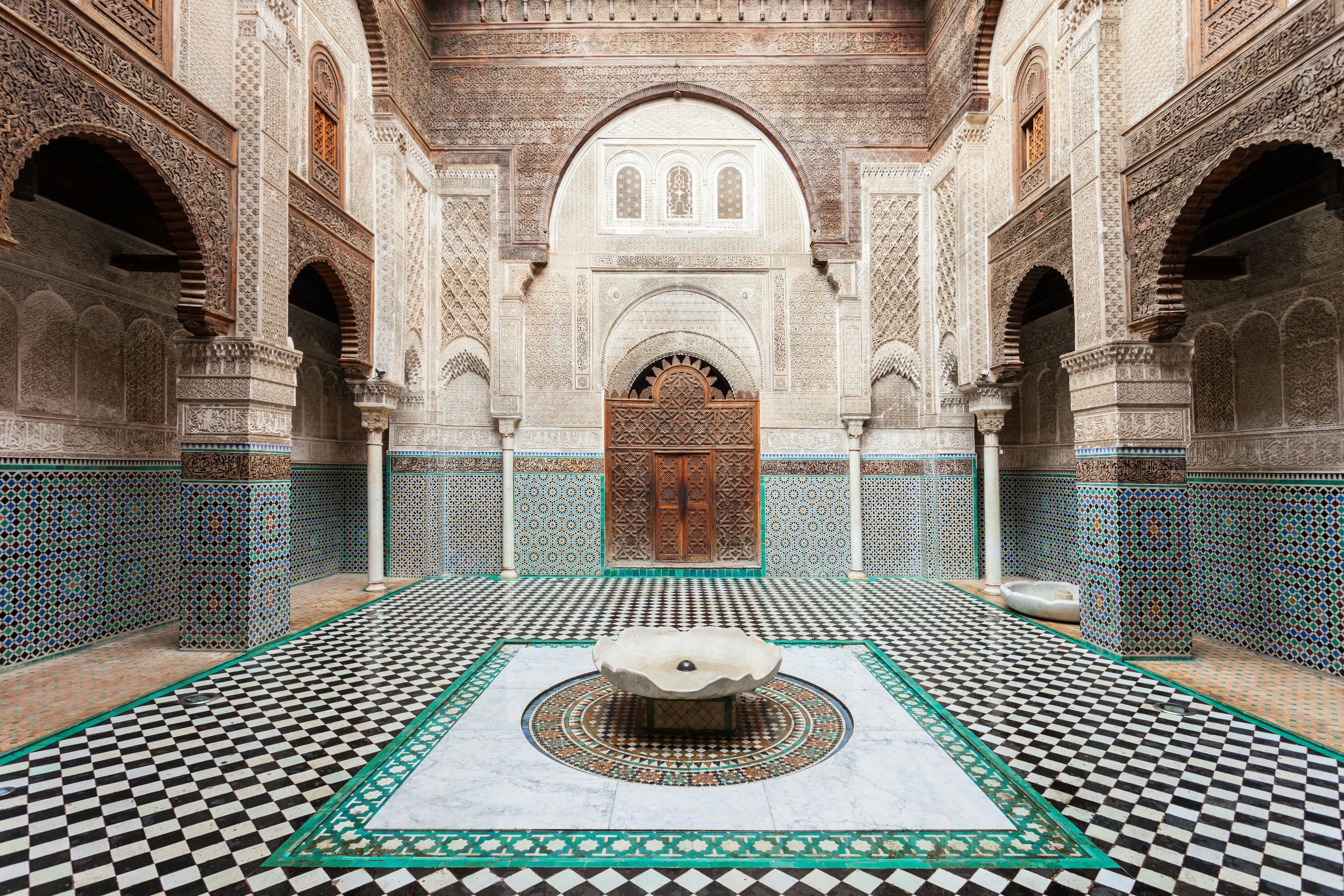 A courtyard in a building with detailed geometric tilework covering the floor, walls and surrounding a carved wooden doorway.