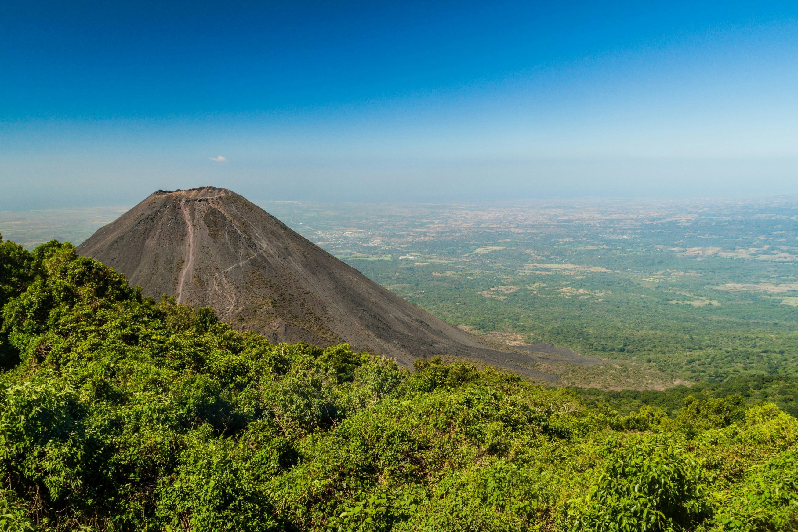 The cinder cone of a volcano juts from its green surroundings